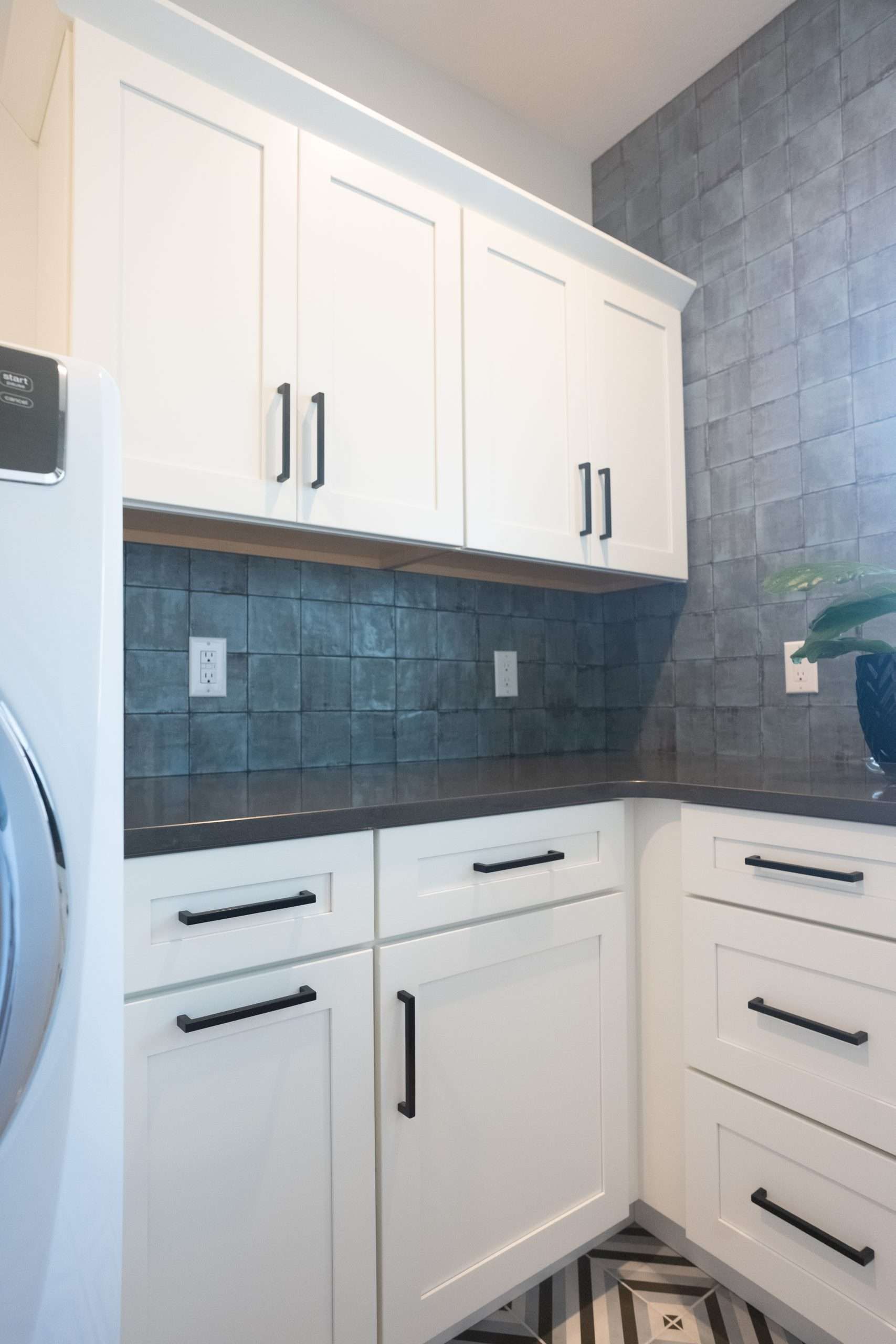 White kitchen corner with cabinets, gray tiled backsplash, and black hardware