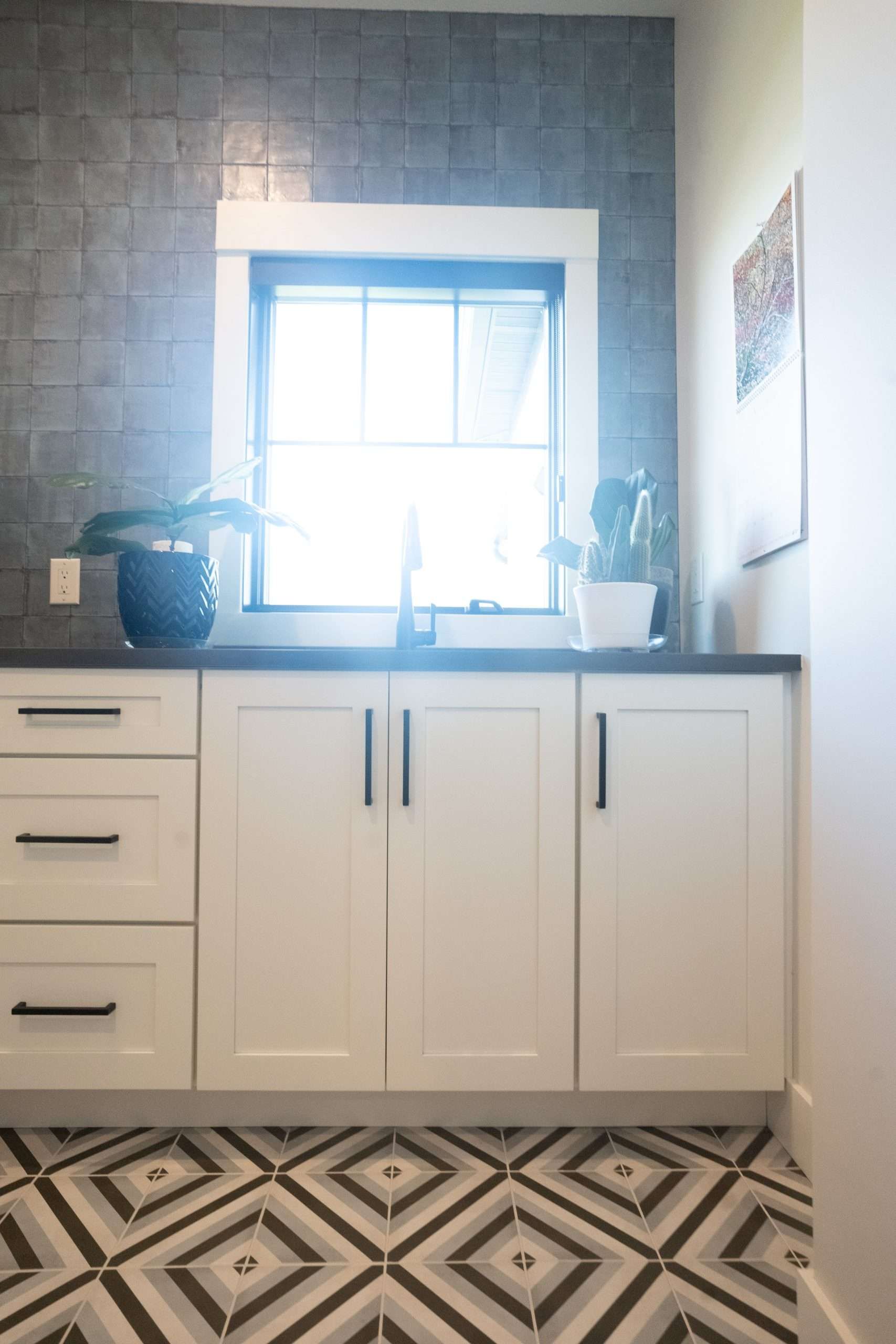 Modern kitchen with white cabinets, gray tile backsplash, and patterned black-and-white floor under a bright window