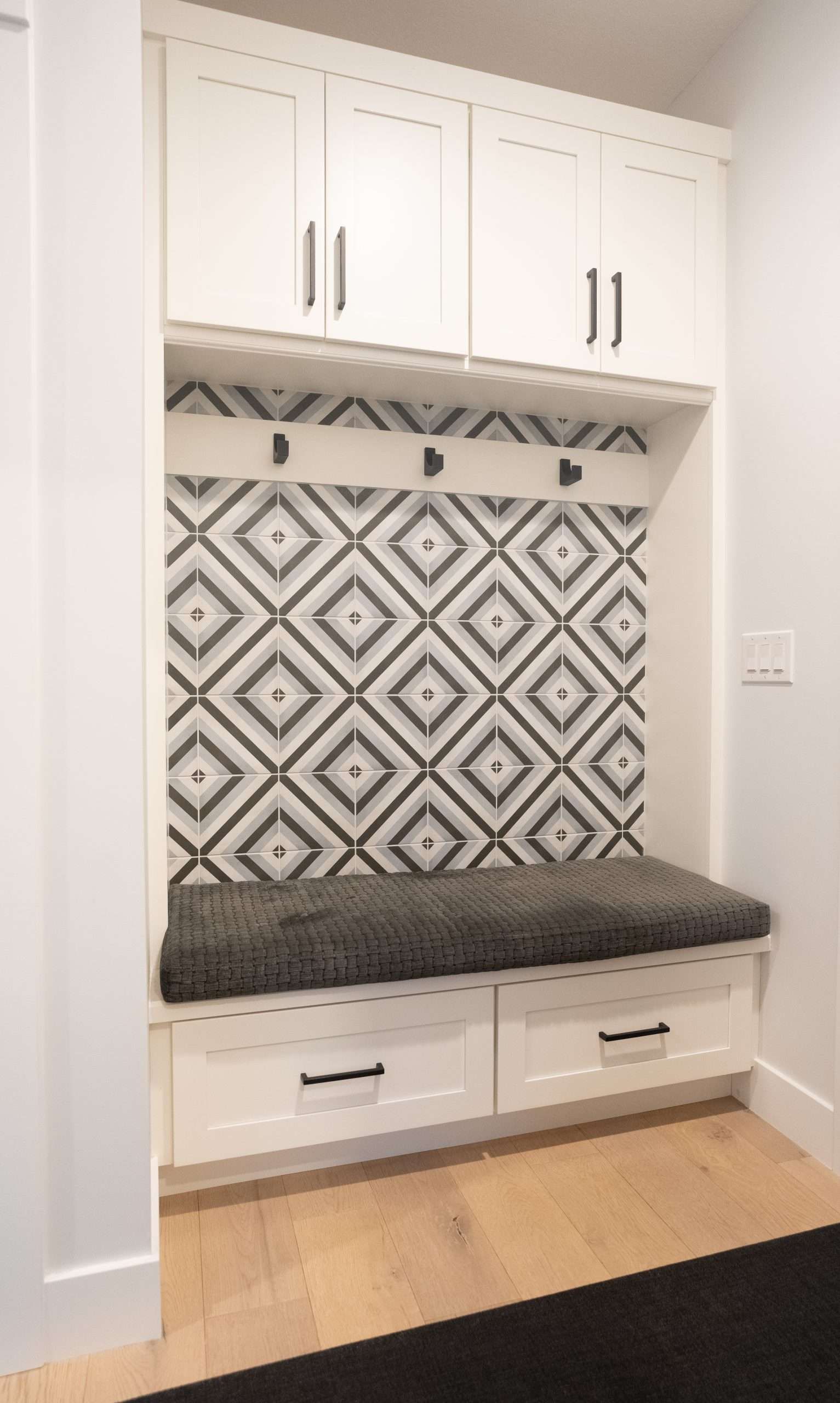 Built-in mudroom bench with white cabinets, patterned tile backsplash, and gray cushion seat