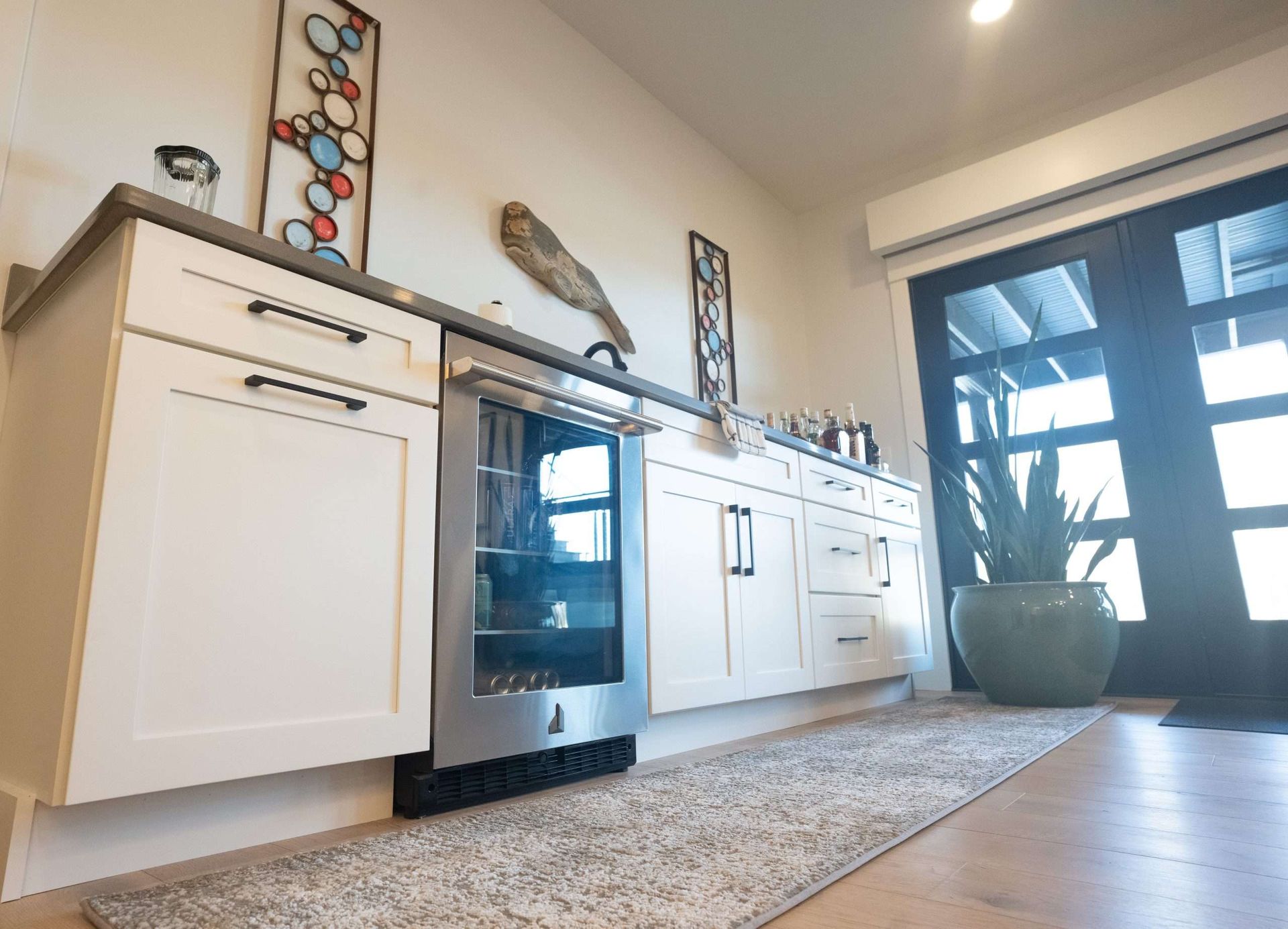 Modern kitchen with white cabinets, black oven, rug, plant, and glass door to the patio