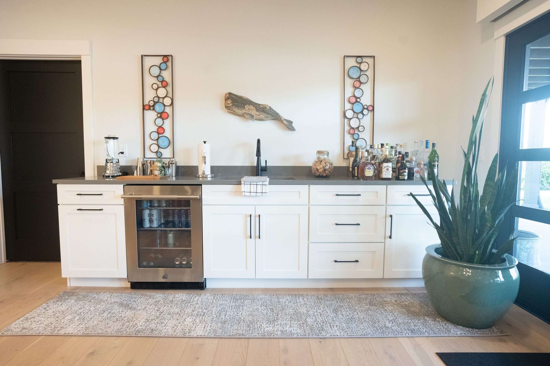 Modern home bar cabinet with wine fridge, decor, and a large potted plant in a bright room