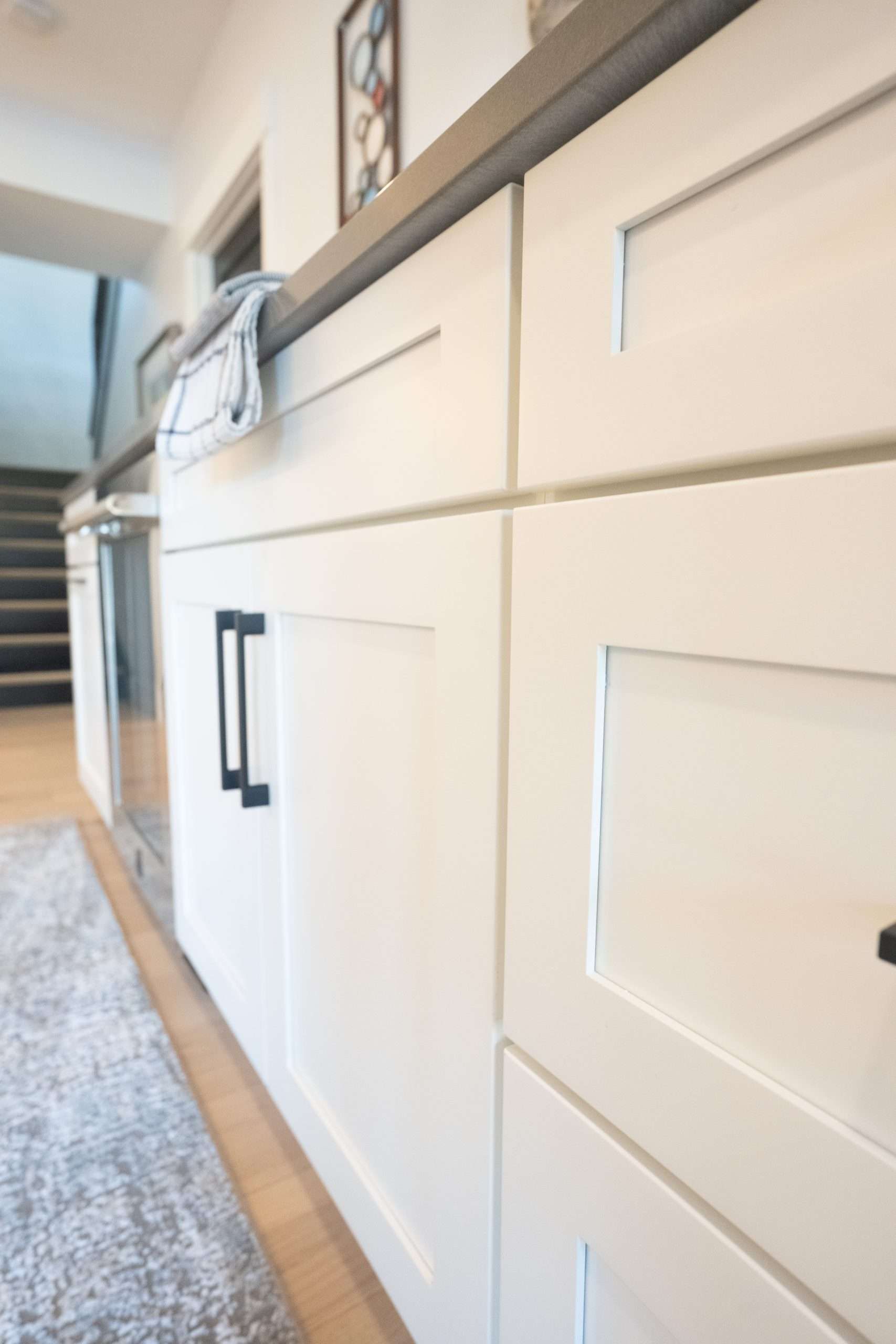 White kitchen cabinets with black handles and a light wood countertop in a bright interior hallway.