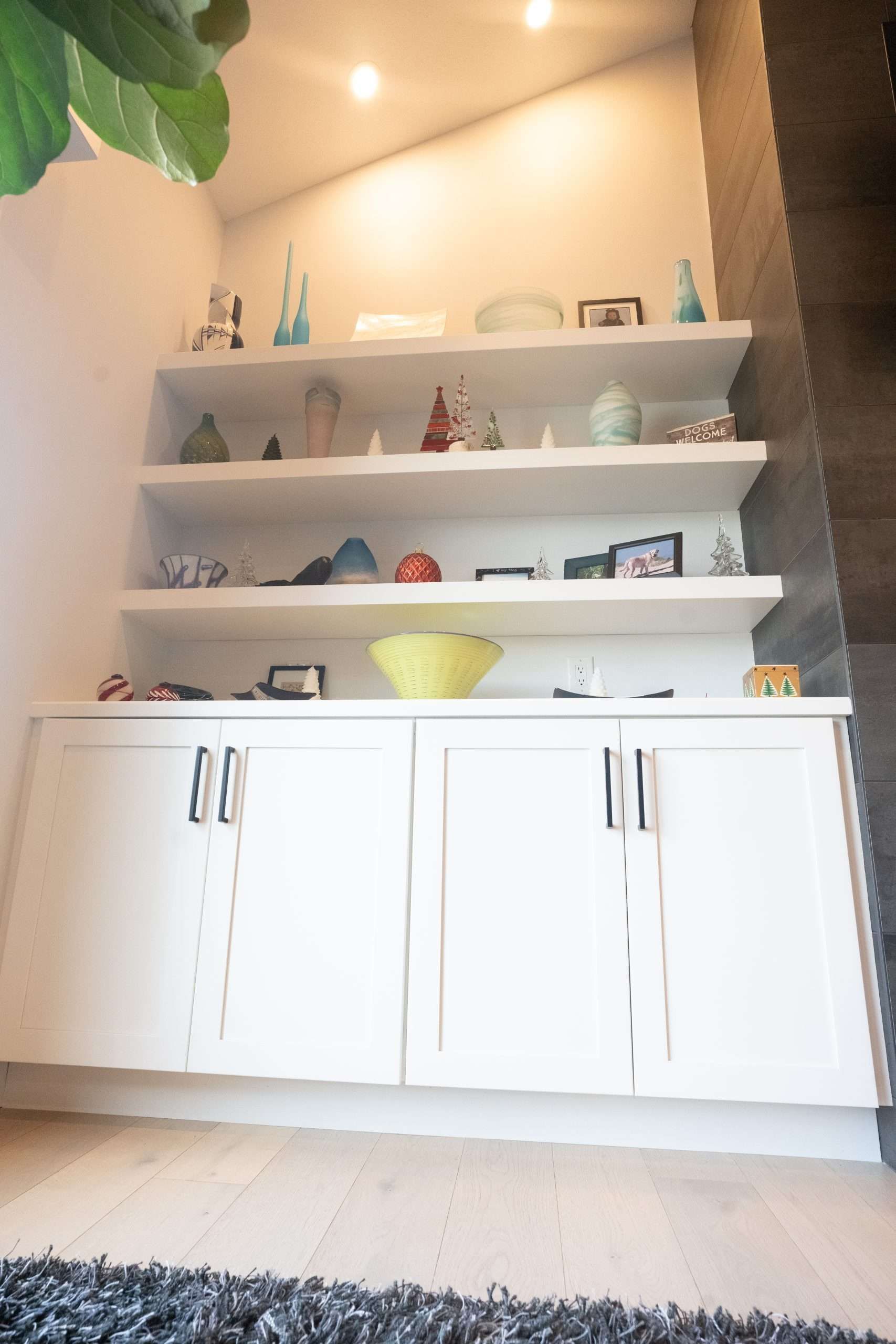 White wall shelves with small decor above a cabinet in a room, with a yellow bowl centered on the middle shelf.