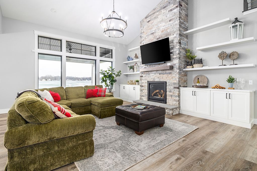 Bright living room with green sectional sofa, stone fireplace, wall TV, and white built-in shelves