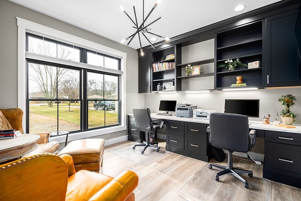 Modern home office with large window, black desk, office chairs, and yellow sofa seating area