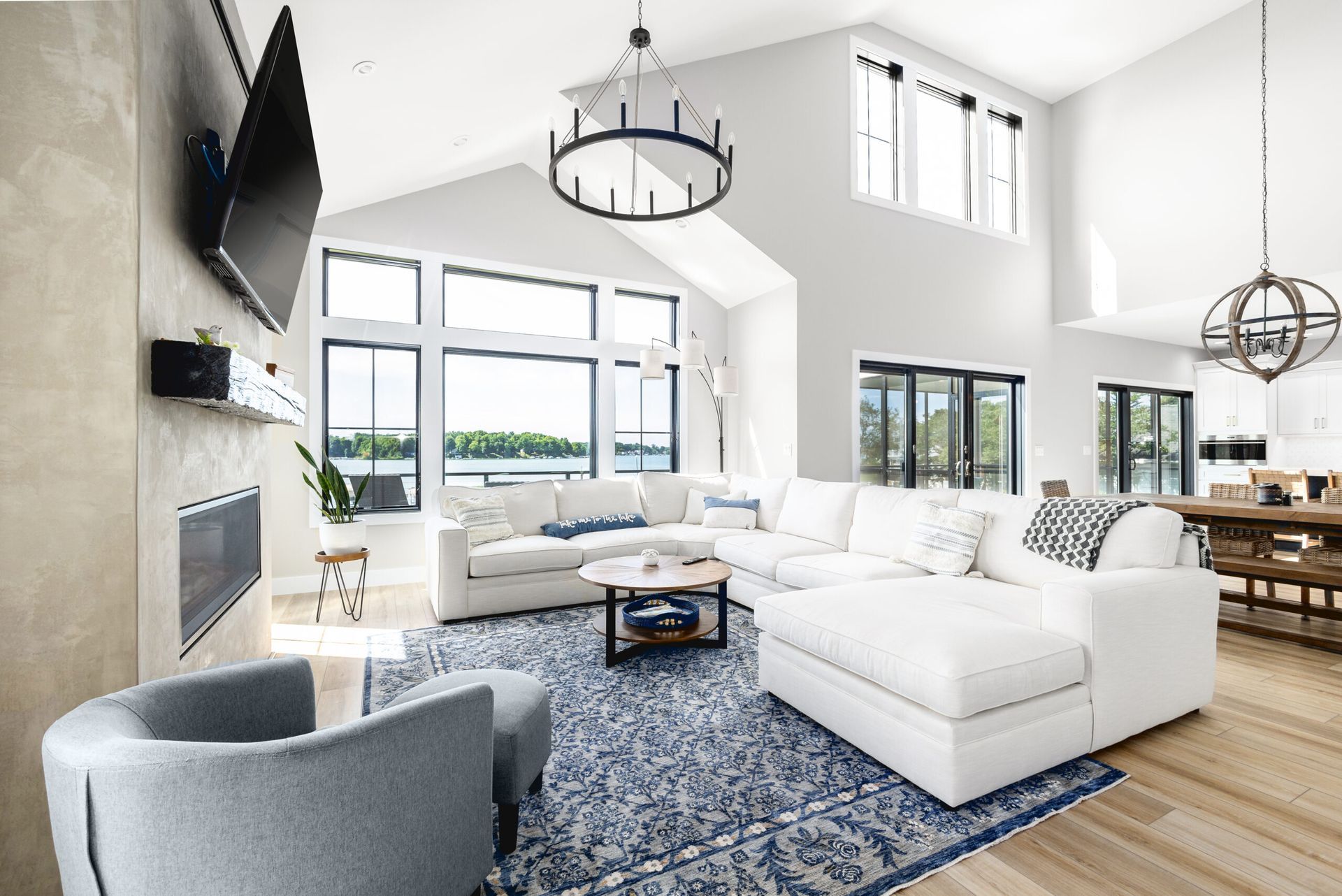 Bright modern living room with white sofas, blue rug, large windows, and a wall-mounted TV