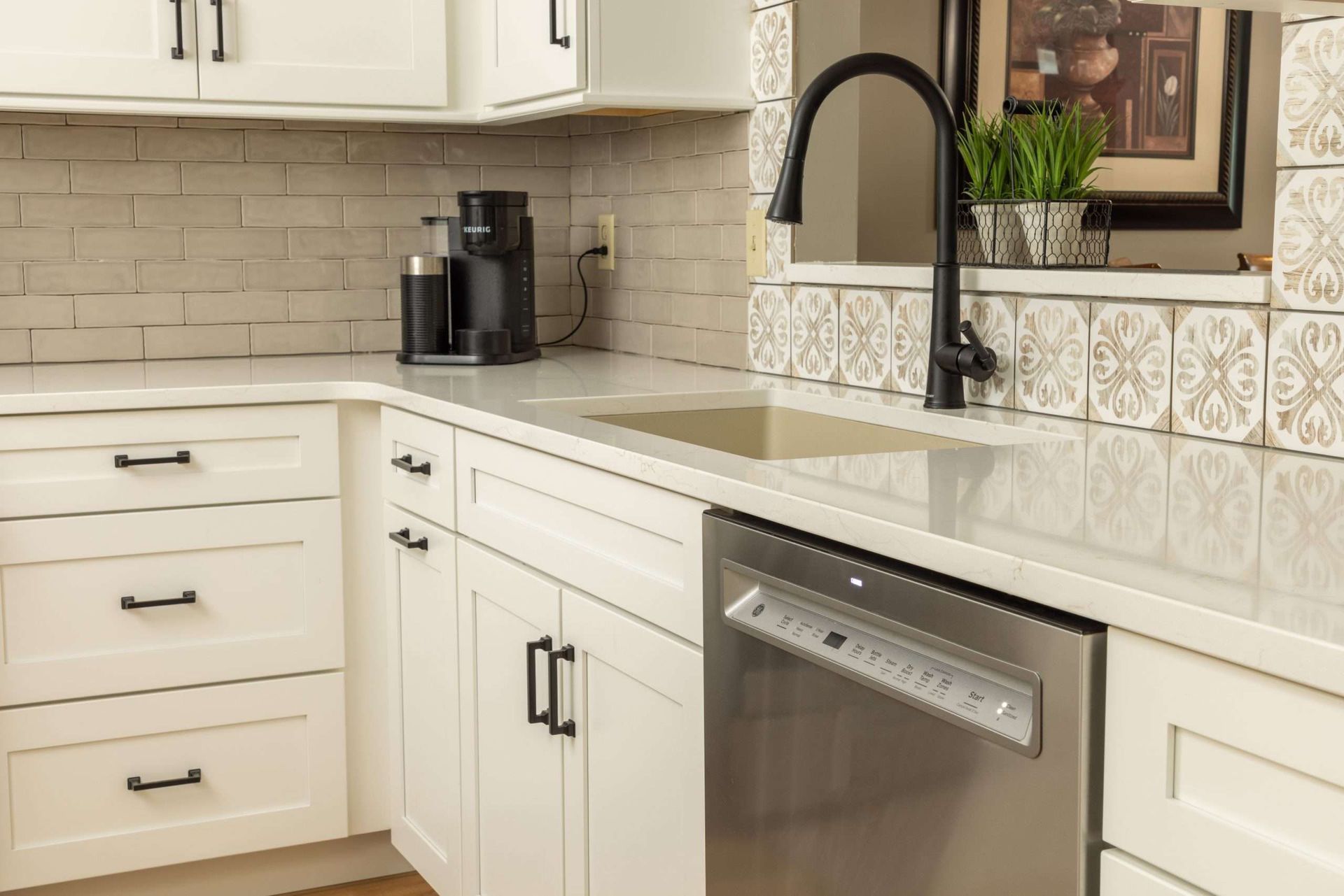 Modern white kitchen with black faucet, marble countertop, subway tile backsplash, and stainless dishwasher