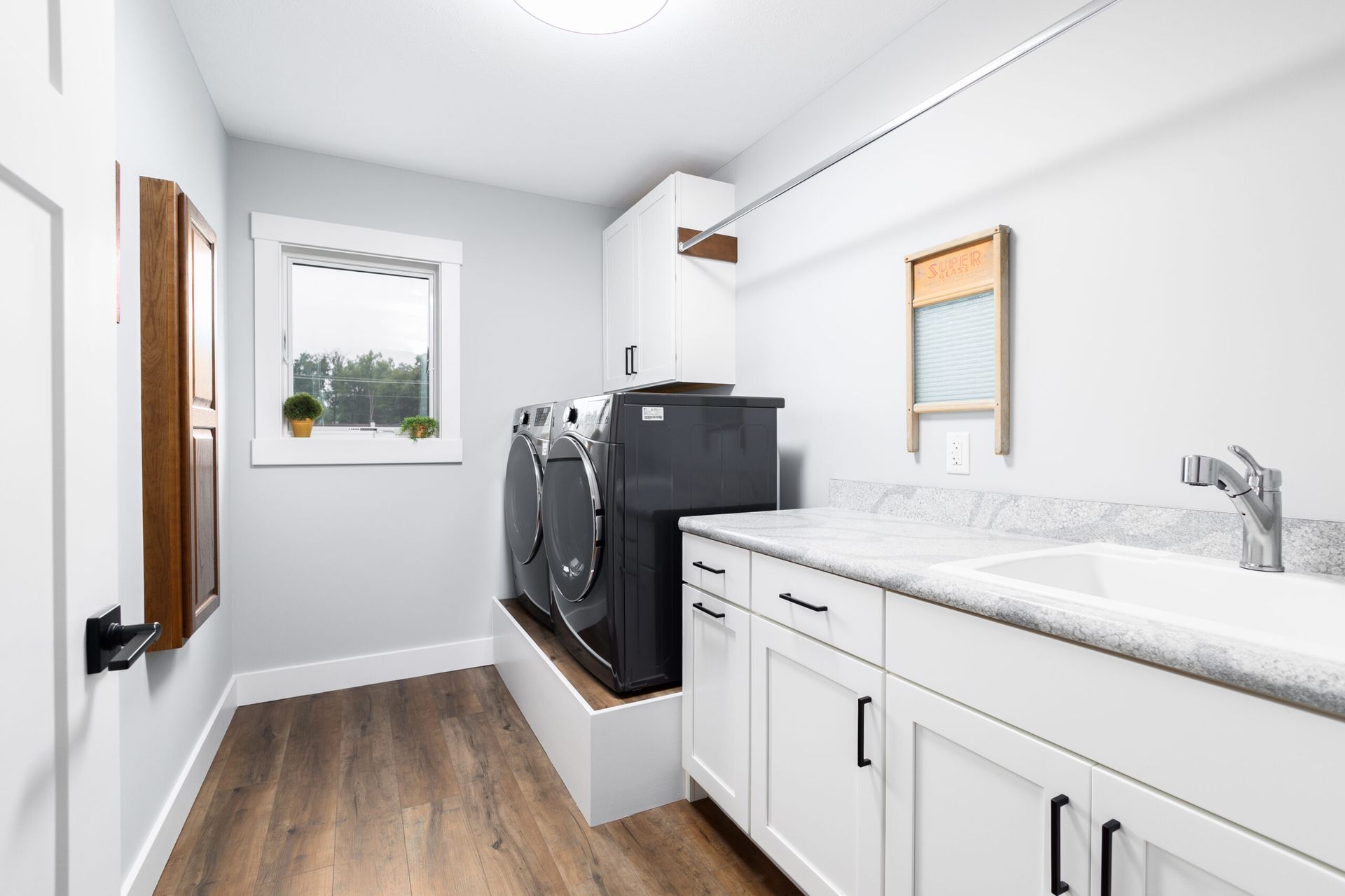 Bright laundry room with washer and dryer, white cabinets, sink, and wood-look floor.