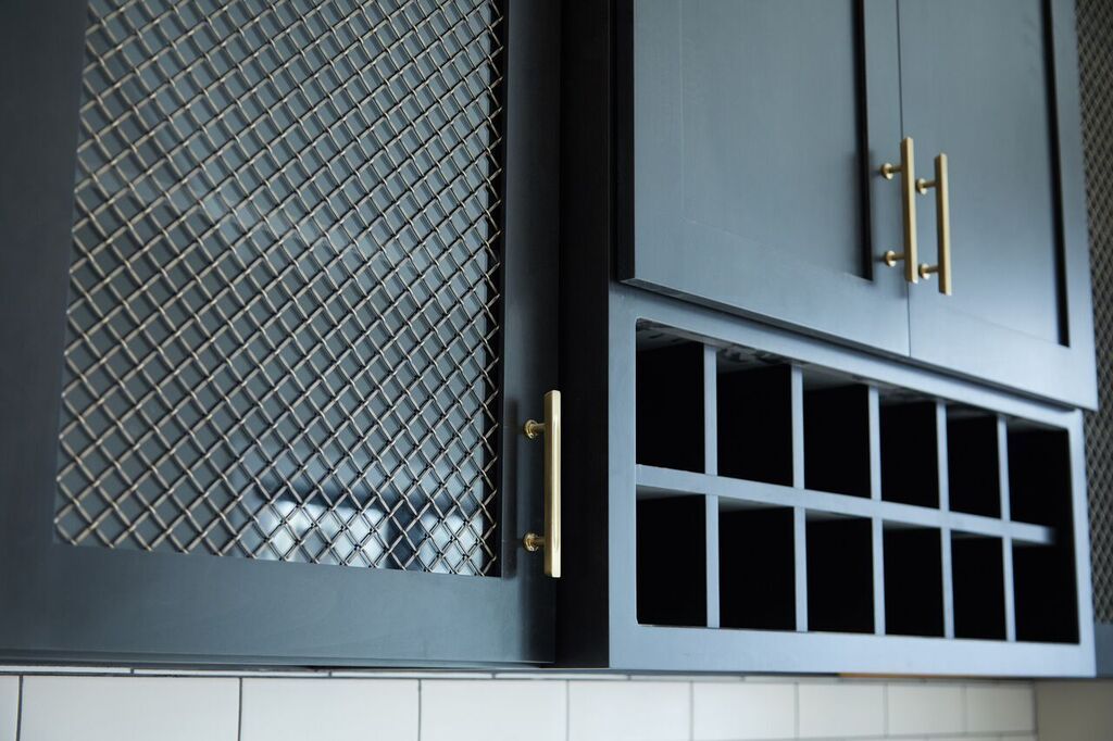Black kitchen cabinets with gold handles and a white cubby shelf against a tiled wall.
