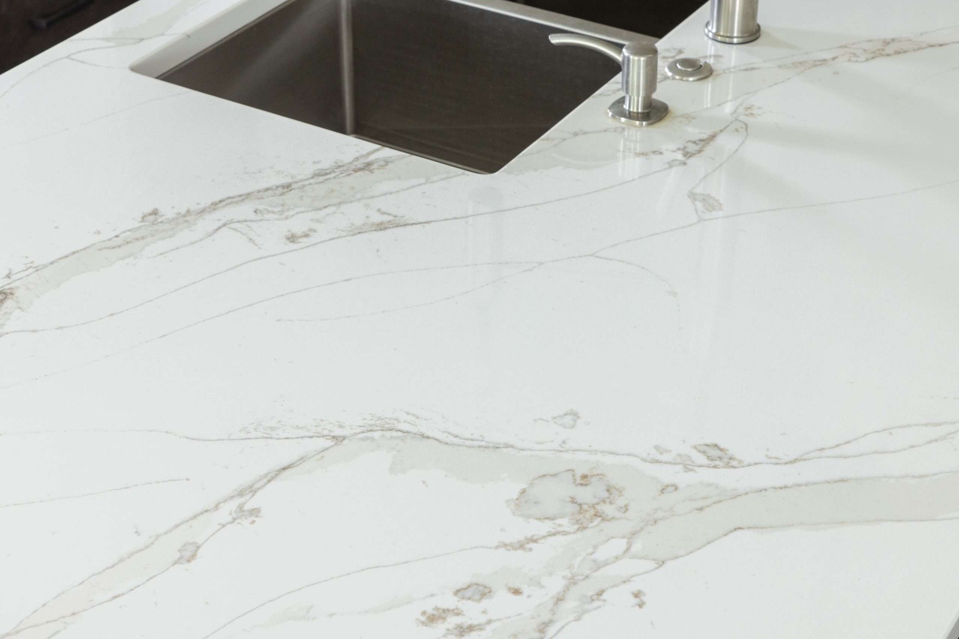 White marble kitchen countertop with a stainless steel sink and faucet, showing water streaks and stains