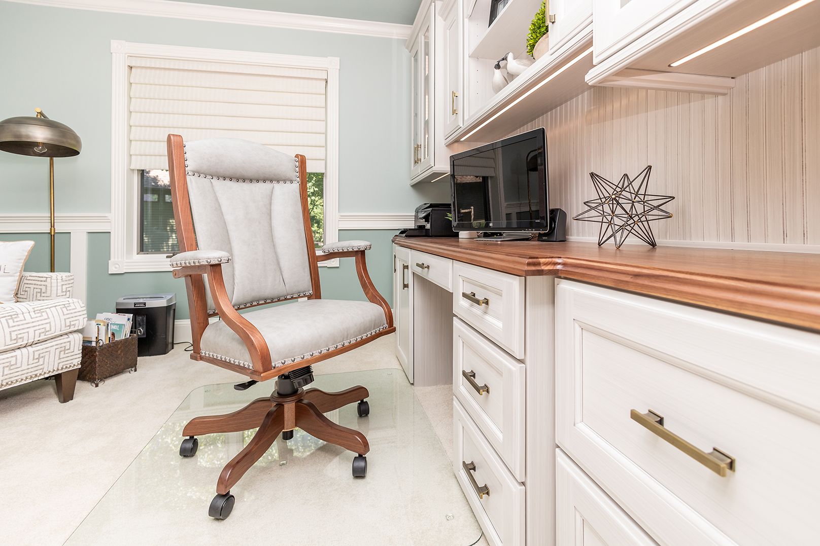 Bright home office with white desk, swivel chair, wood countertop, and computer against pale green walls.