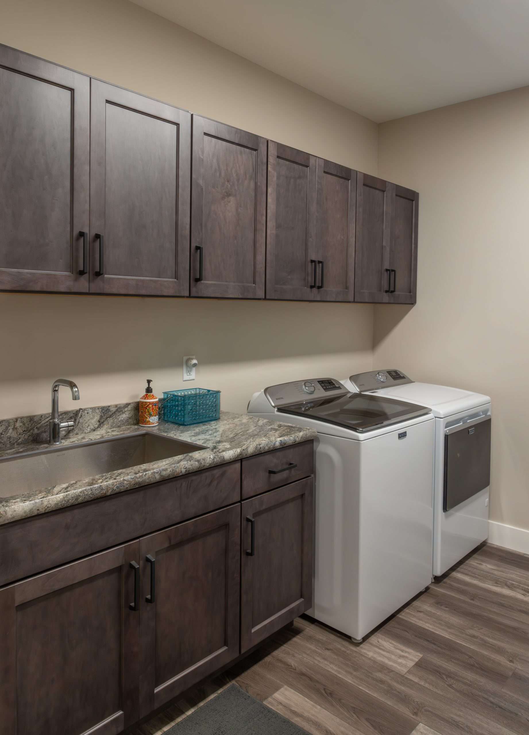Modern kitchenette with dark wood cabinets, granite counters, sink, stove, and white appliances.