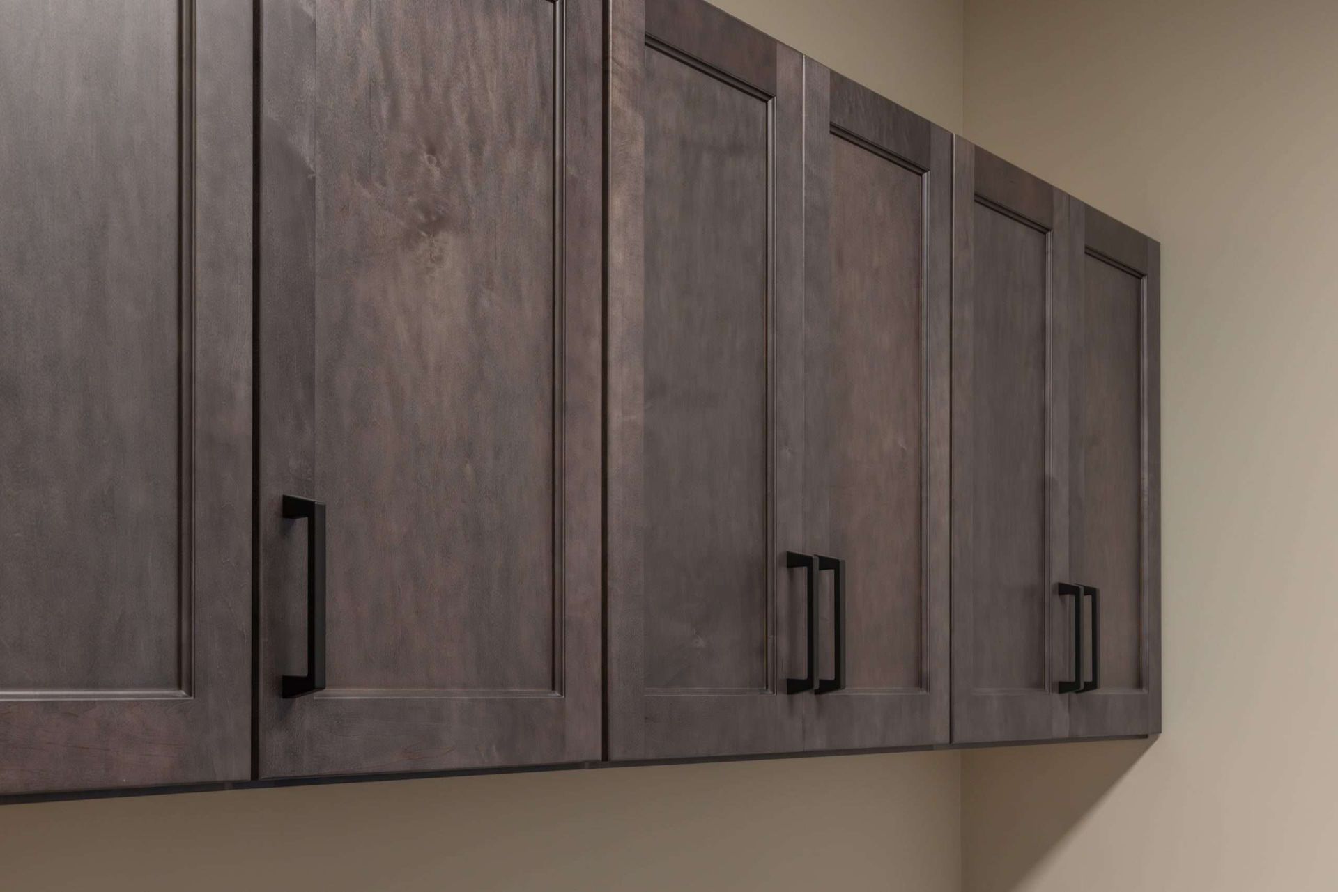 Row of dark wood kitchen cabinets with black handles against a beige wall