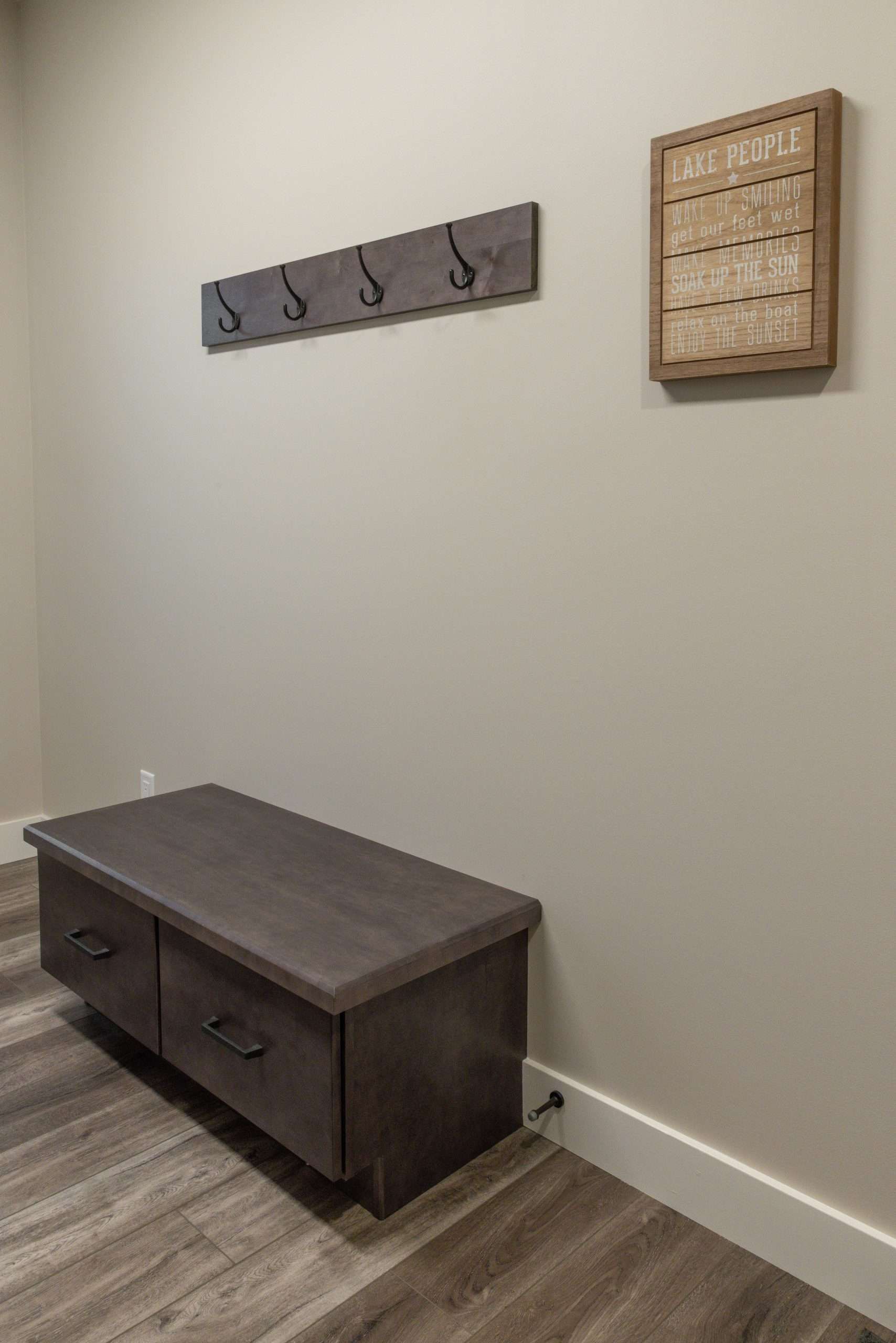Small entryway with a dark bench, wall hooks, and a woven wall organizer on a beige wall.