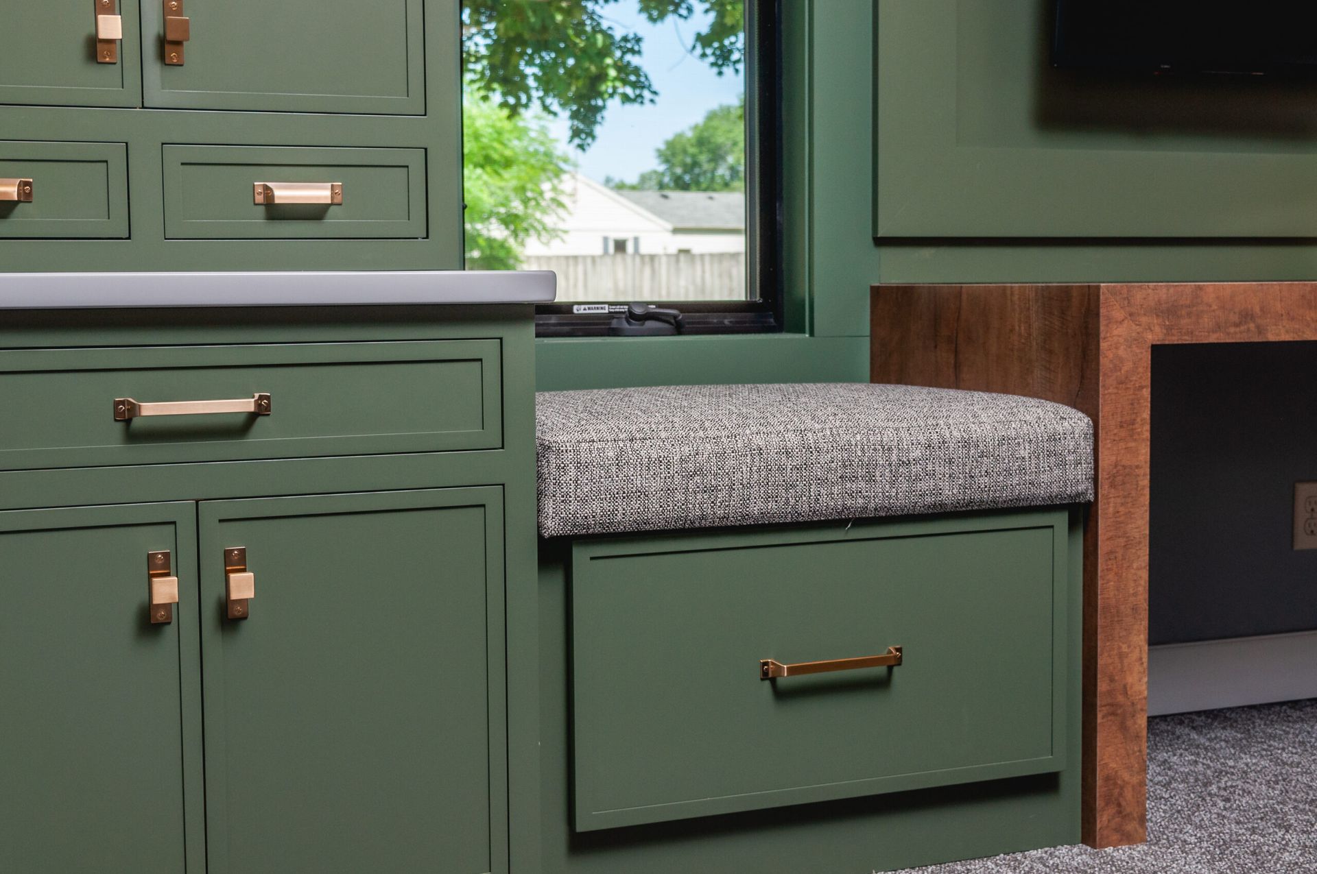 Green cabinets with brass pulls, speckled countertop, and a window in a small kitchen nook