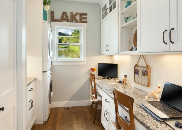 Bright home office with built-in white cabinets, wood desk, and “LAKE” sign above a window