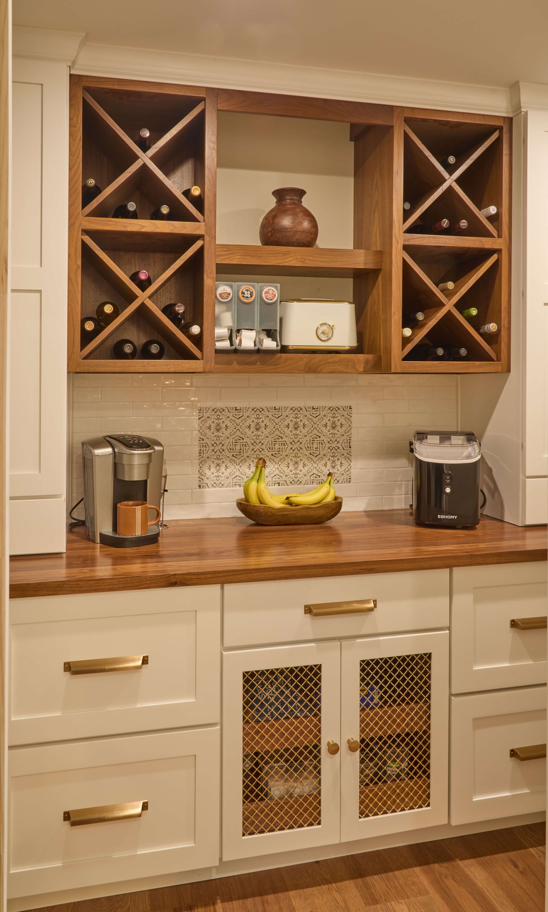 Kitchen countertop with coffee maker, bananas, and built-in wine racks above cream cabinets