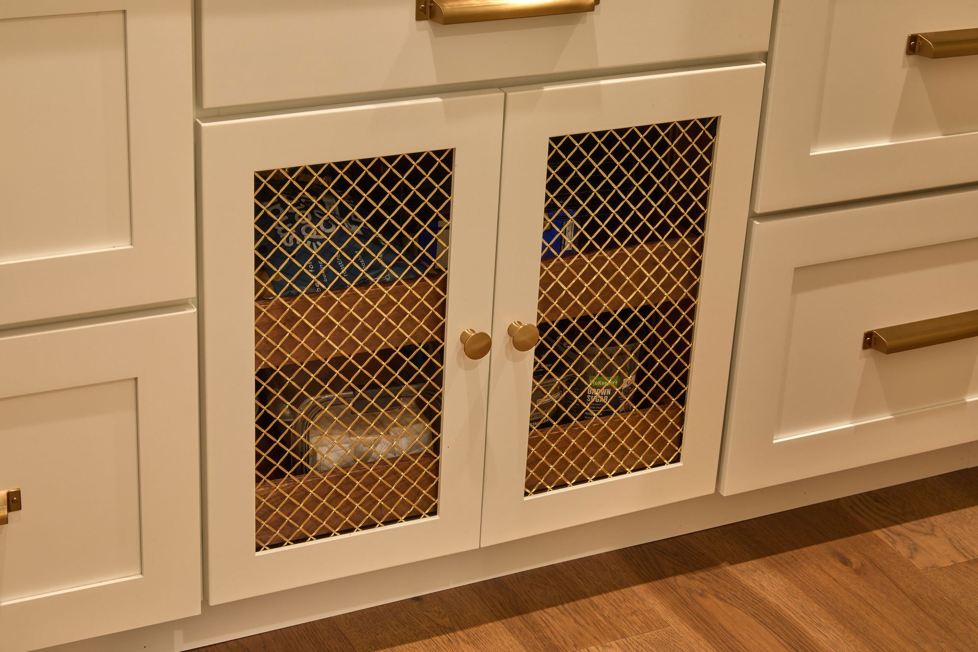 White kitchen cabinet with mesh doors, showing a cat resting inside behind the screen.