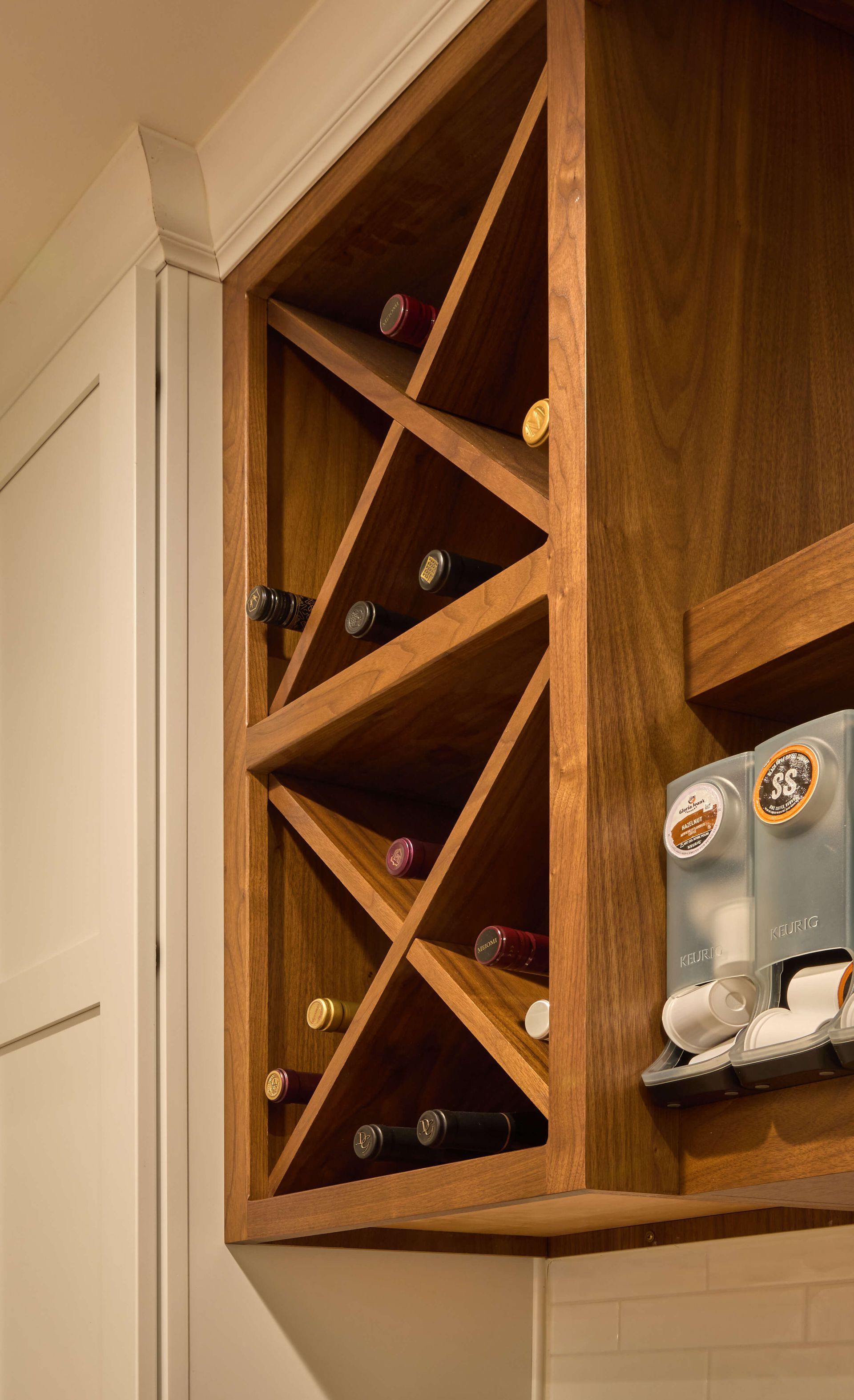 Wooden kitchen wine rack with diagonal slots holding several bottles beside a silver coffee machine.