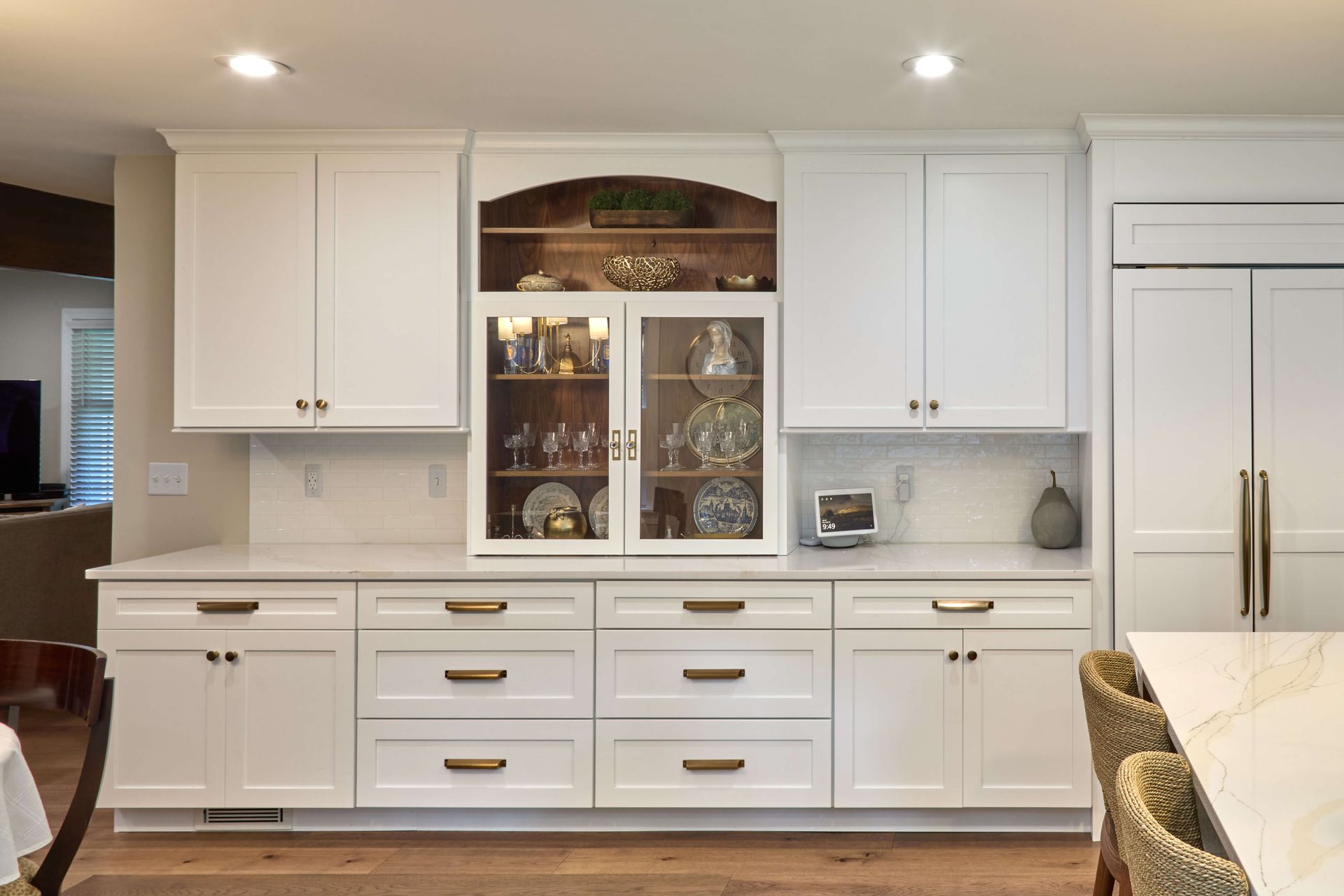 White kitchen cabinetry with glass display cabinets and gold handles under recessed lights