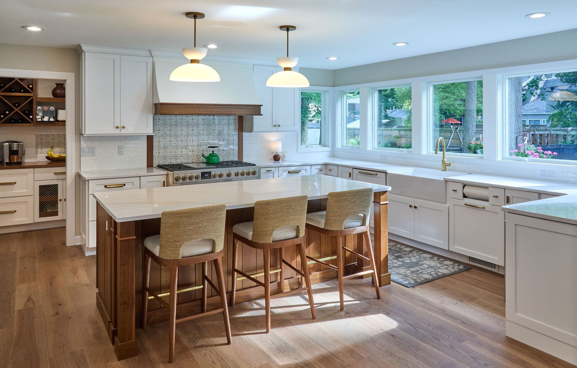 Bright modern kitchen with white cabinets, large island, bar stools, pendant lights, and sunlit windows