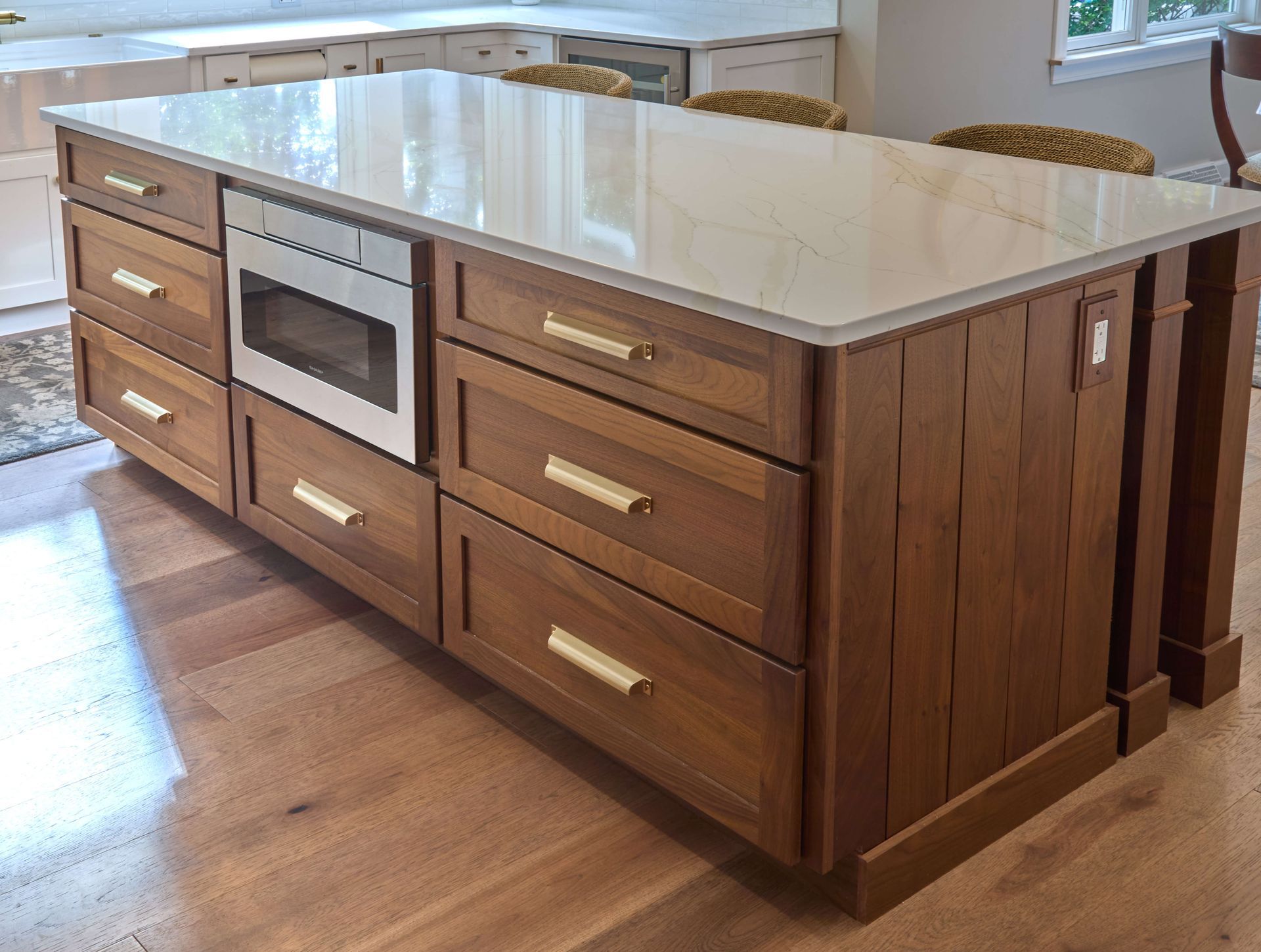 Large wooden kitchen island with white countertop and built-in oven, shown in a bright kitchen.