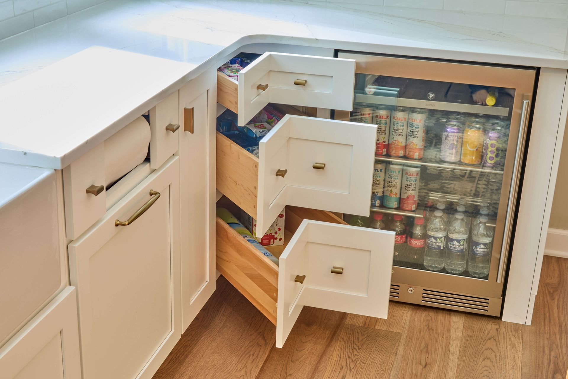 Open fridge drawers under a white counter, revealing drinks and produce in a kitchen.