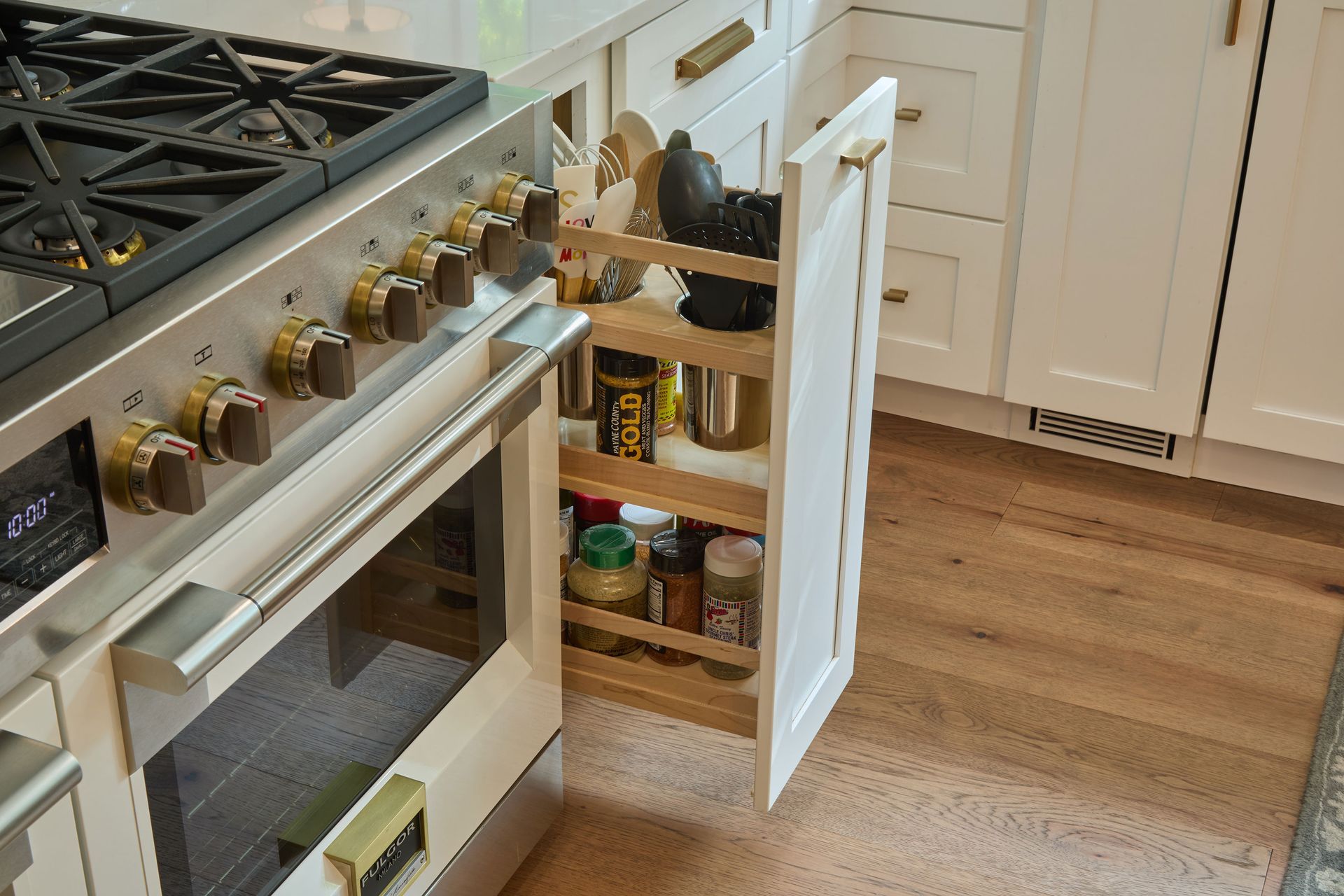 Open kitchen cabinet with spices and jars beside a stainless steel stove and hardwood floor