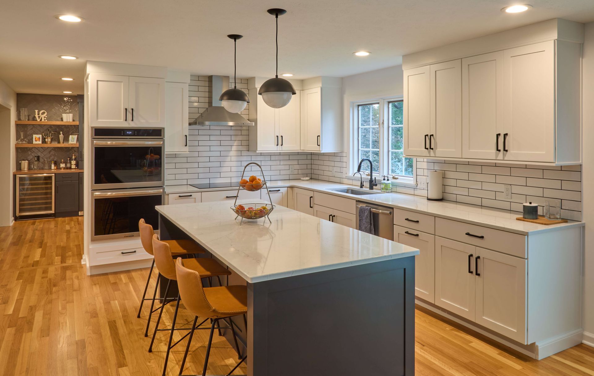 Modern kitchen with white cabinets, island seating, pendant lights, and hardwood floors
