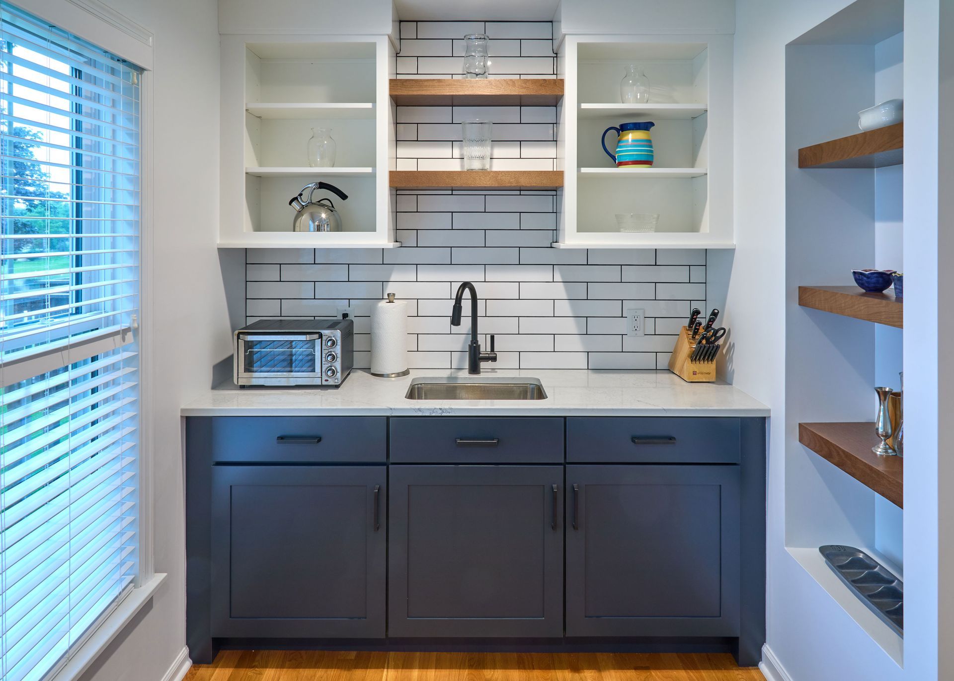 Modern kitchen nook with navy cabinets, white shelves, subway tile, and wooden accents