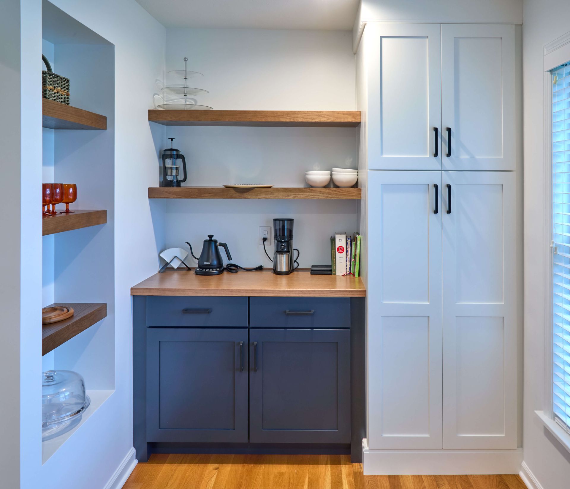 Modern kitchen nook with blue cabinets, white shelves, wood countertops, and appliances on display