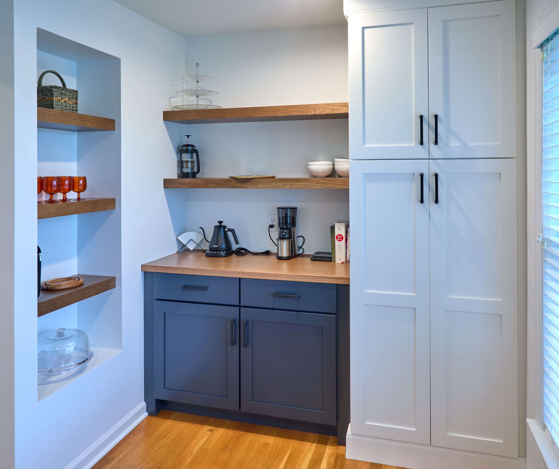 Compact kitchen nook with white cabinets, dark lower cabinets, wooden shelves, and coffee maker on the counter.