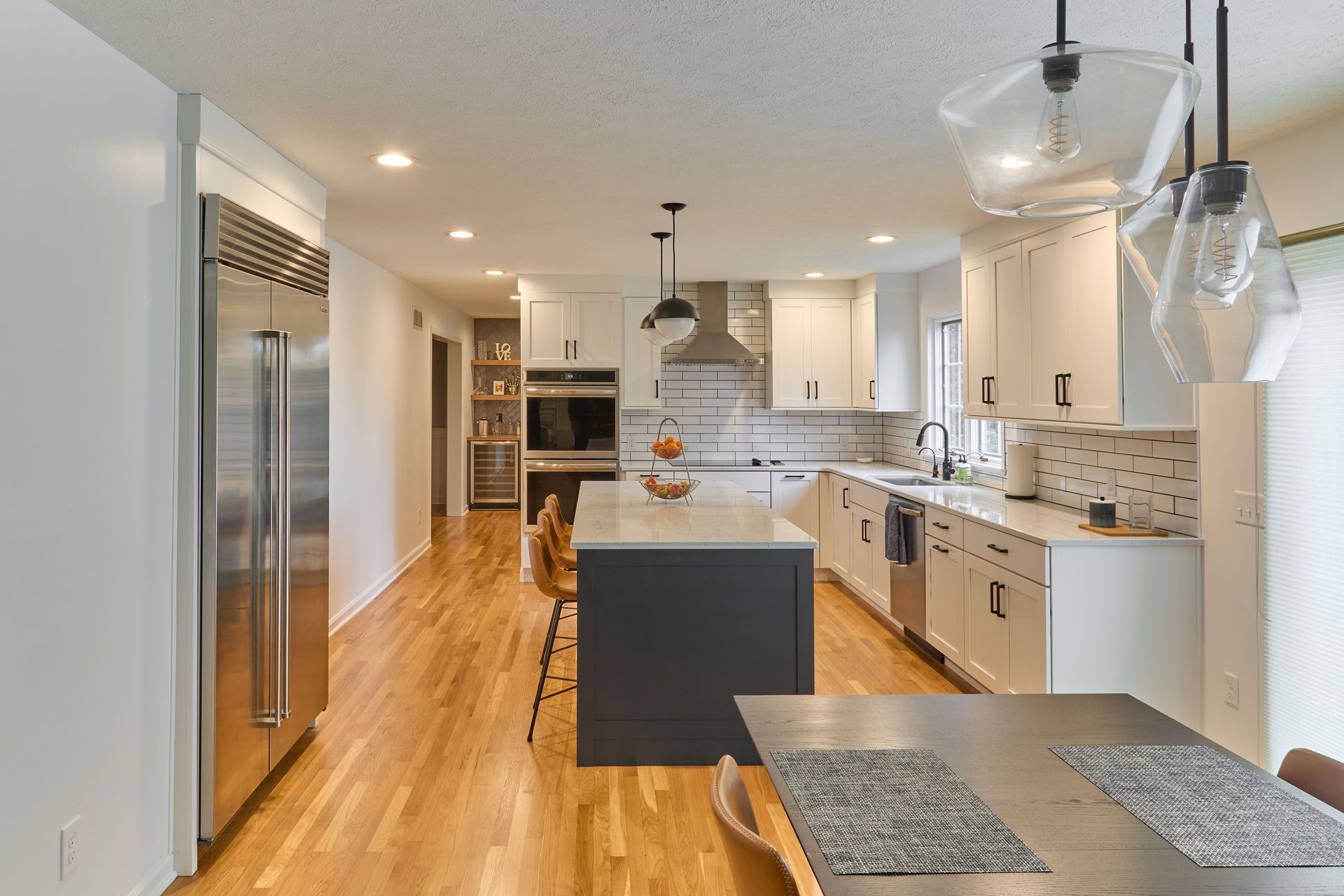 Bright modern kitchen with island, stainless fridge, white cabinets, and hardwood floors