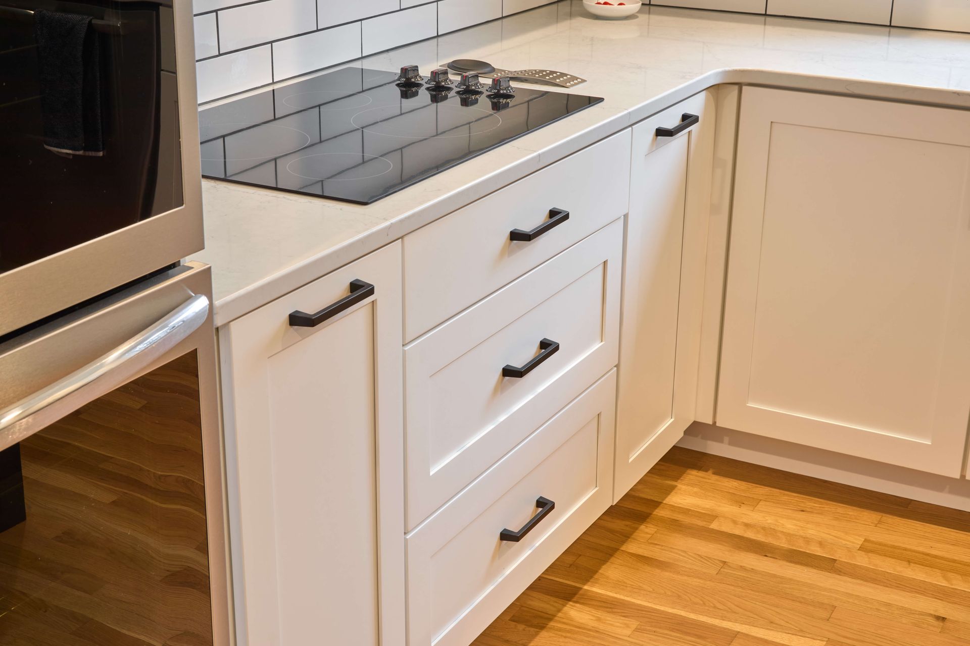 White kitchen cabinets and countertop with built-in stove and oven, hardwood floor, and black hardware