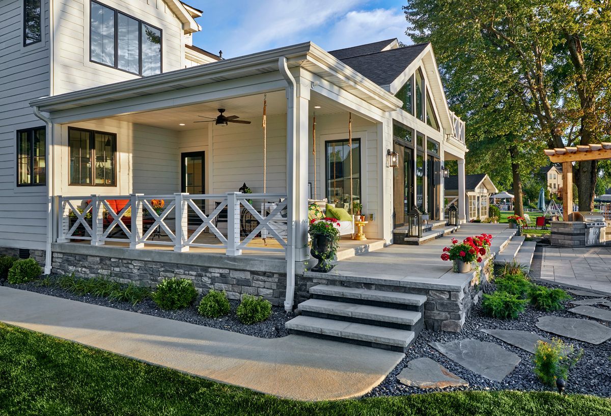 White house with a covered front porch, steps, and landscaped garden in bright daylight