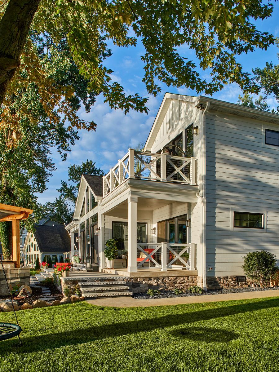 White two-story house with porch and balcony in a sunny landscaped yard