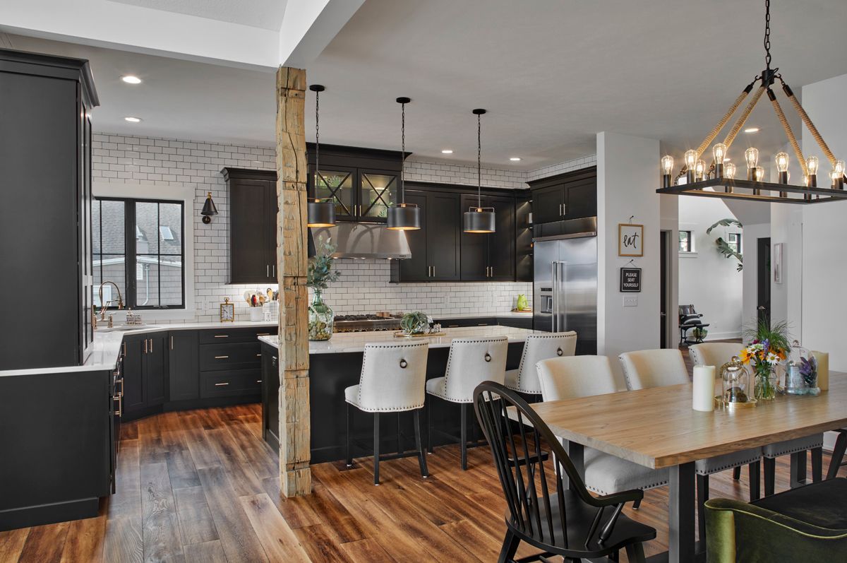 Bright open kitchen and dining area with dark cabinets, white island stools, wood floors, and a chandelier
