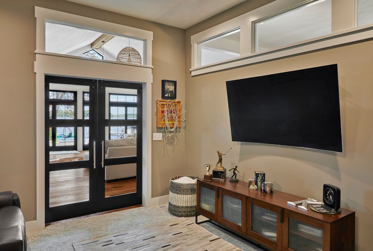 Living room with glass double doors, large wall-mounted TV, and wooden media console with decor