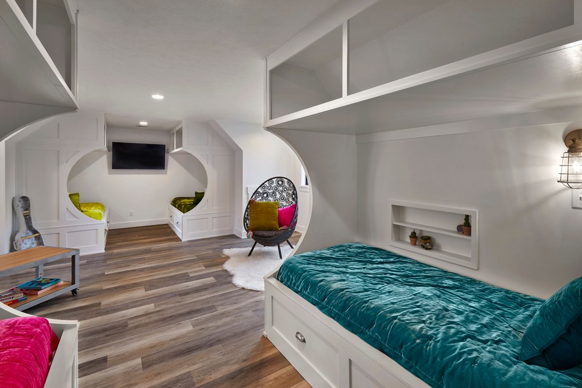 Bright white bedroom with a teal bedspread, wood floor, TV, and two colorful chairs in an arched nook
