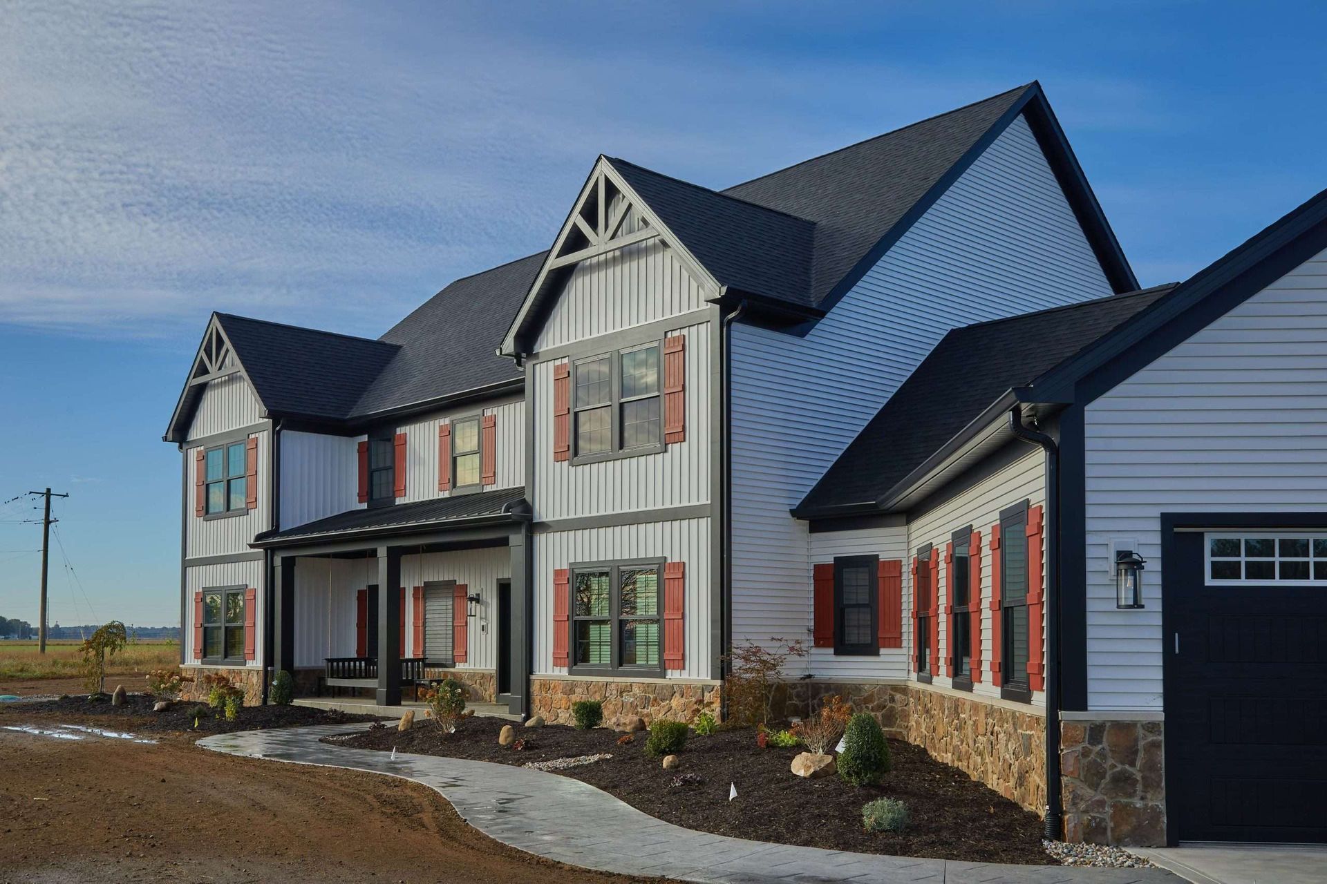 New two-story house with gray siding, red shutters, and stone trim in a rural setting