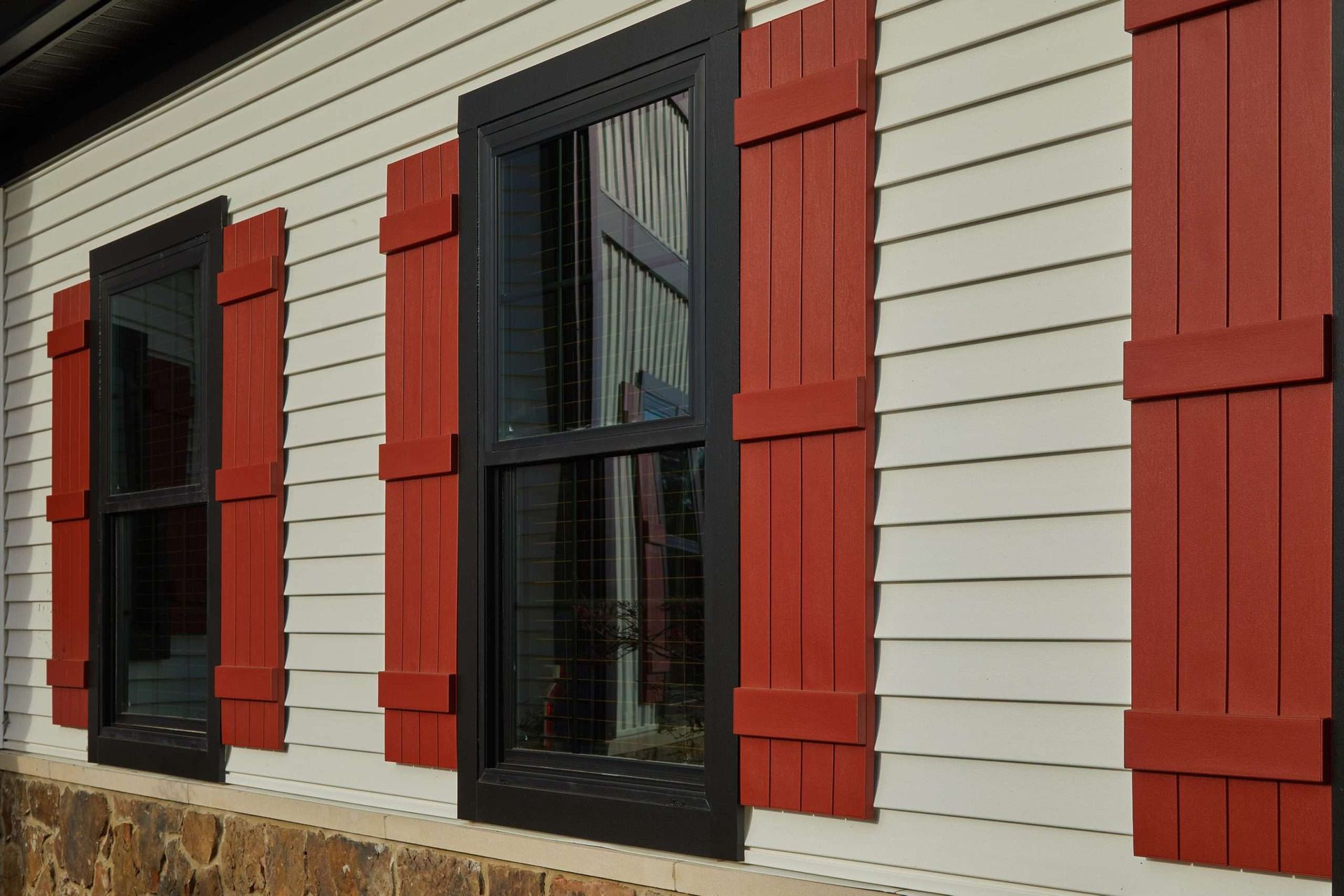 Exterior wall with black-framed windows, red shutters, and white siding above a stone base