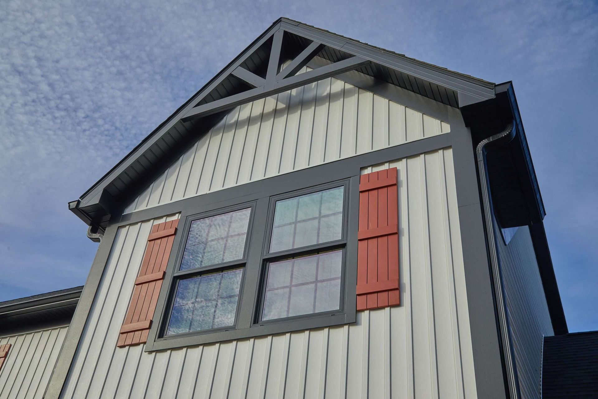 House exterior with gray siding, dark-framed windows, and red shutters under a peaked gable