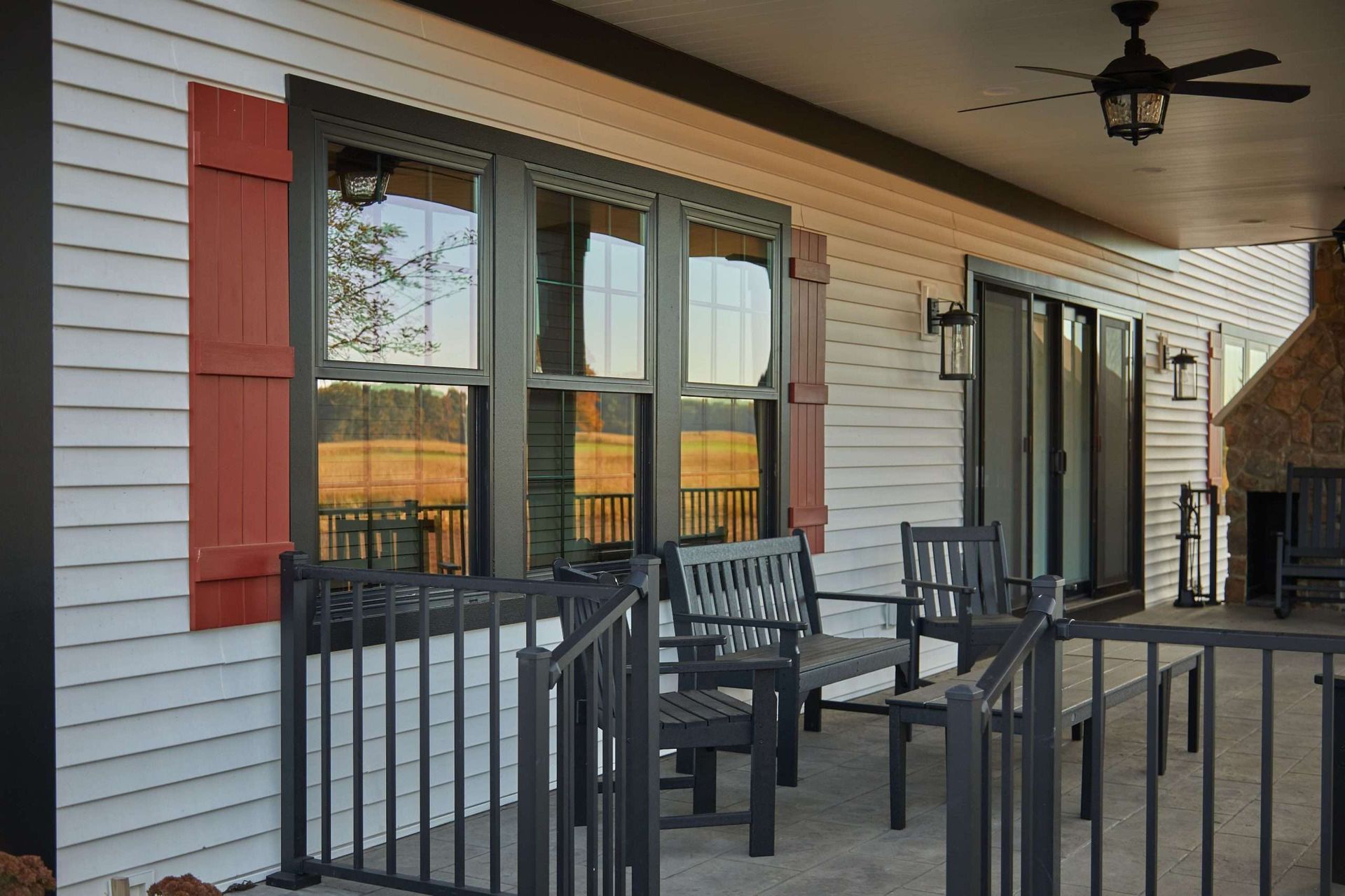 Covered apartment patio with black railings, chairs, and windows with red shutters