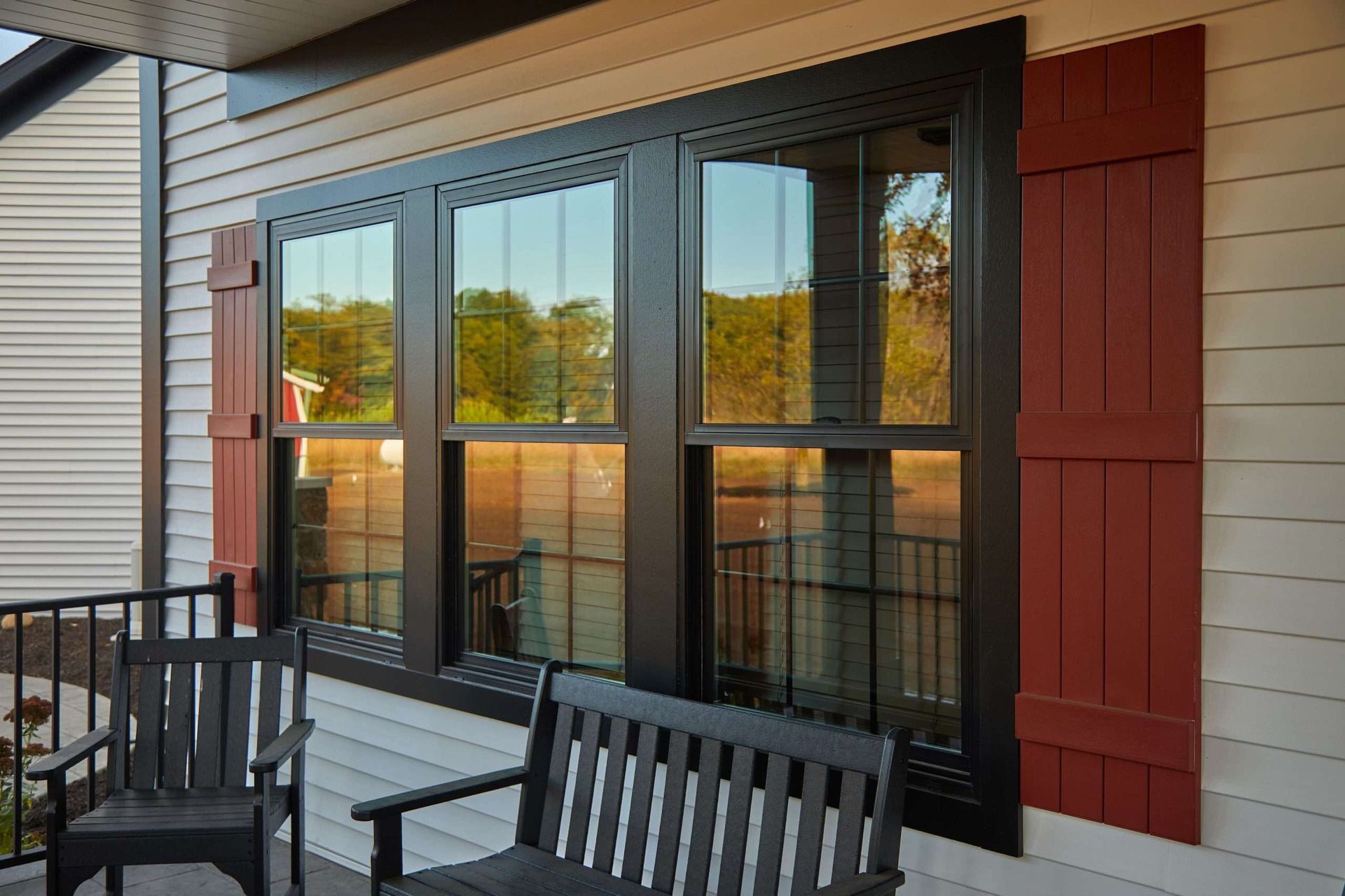 Porch with black railing and chairs beside a brick wall and large reflective windows