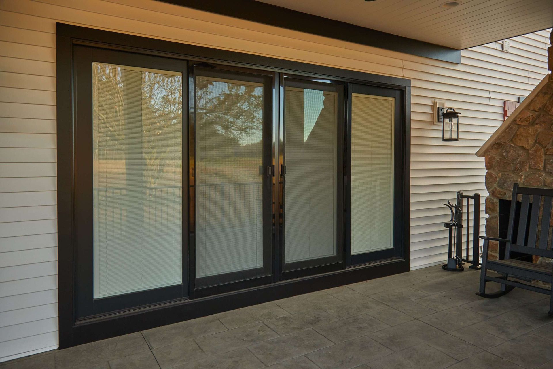 Black-framed patio sliding doors with vertical blinds on a covered outdoor patio.