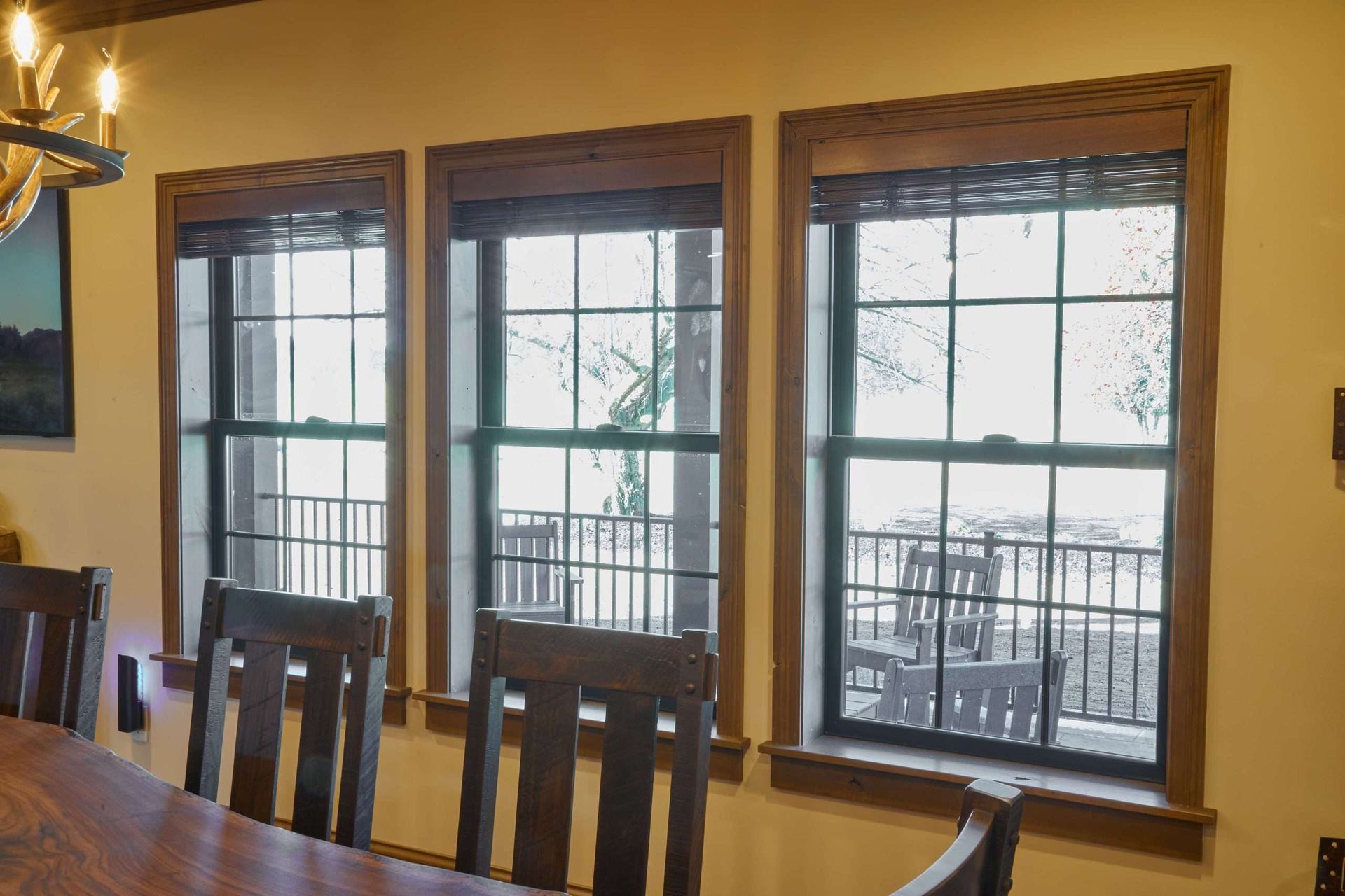 Dining room with wooden table and chairs beside three windows overlooking a balcony in daylight