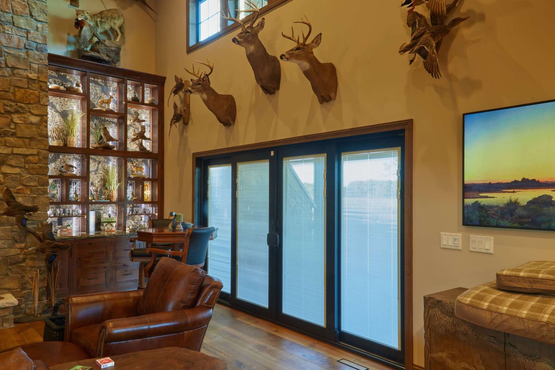 Rustic living room with mounted deer heads, leather chairs, and frosted glass doors opening to a deck.