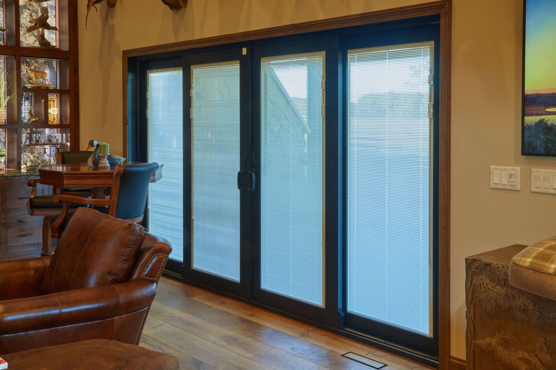 Living room with large black-framed glass doors and blue blinds, wood floors, and a leather chair