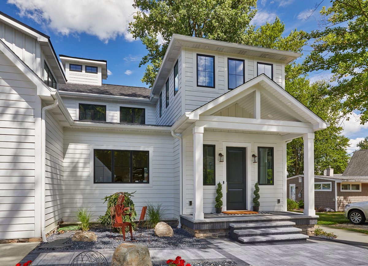 White two-story house with porch, black doors, and stone steps under a blue sky