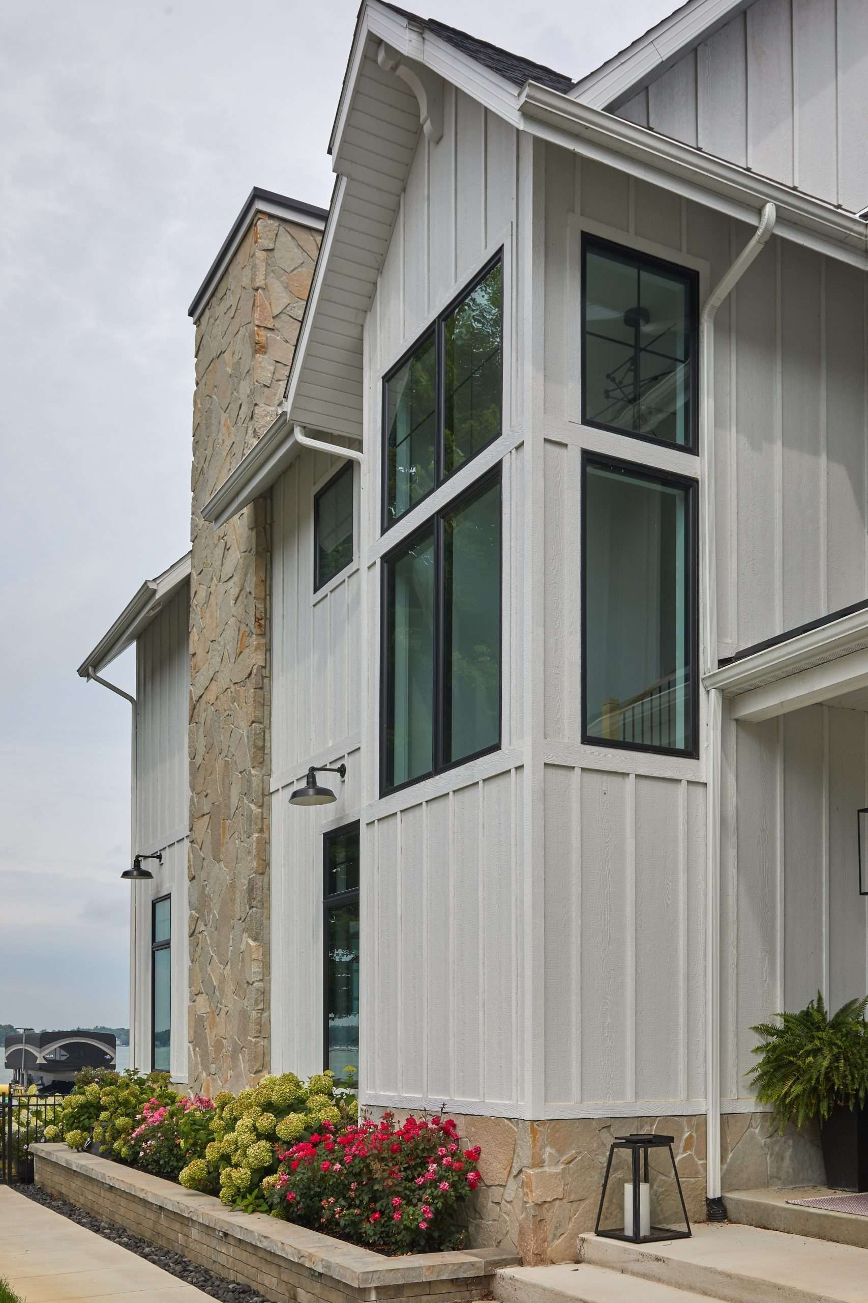 Modern white house exterior with tall windows, stone accents, and flower beds along the front walk